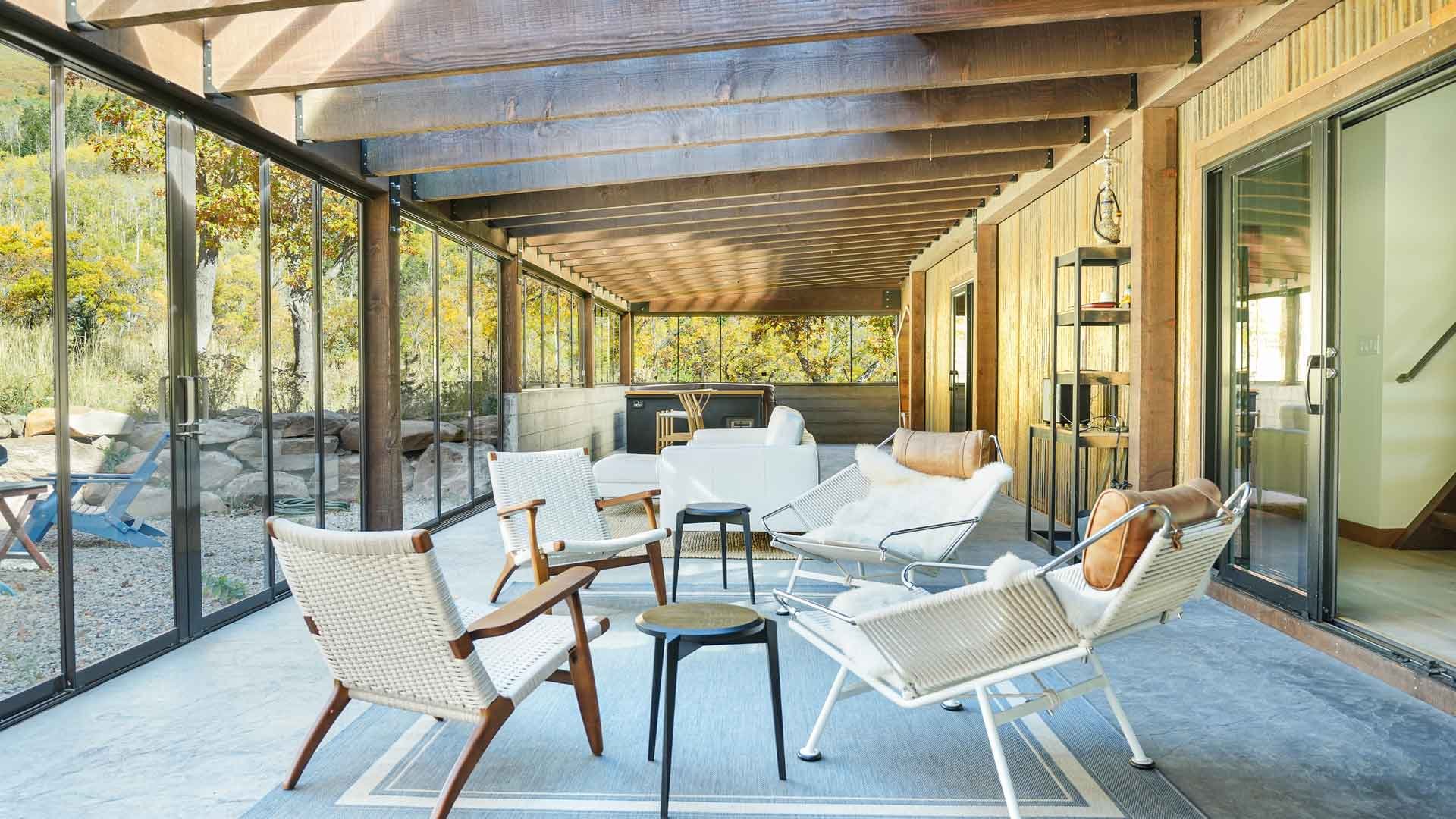 Sunroom with glass walls, wooden ceiling, and outdoor scenery, featuring white and wooden lounge chairs, small black tables, a white couch, and a bookshelf built by general contractors durango