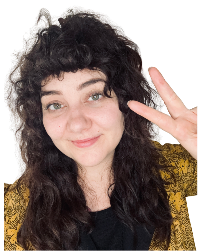 A woman with curly dark hair making a peace sign with her hand, smiling at the camera, wearing a patterned yellow and black top.