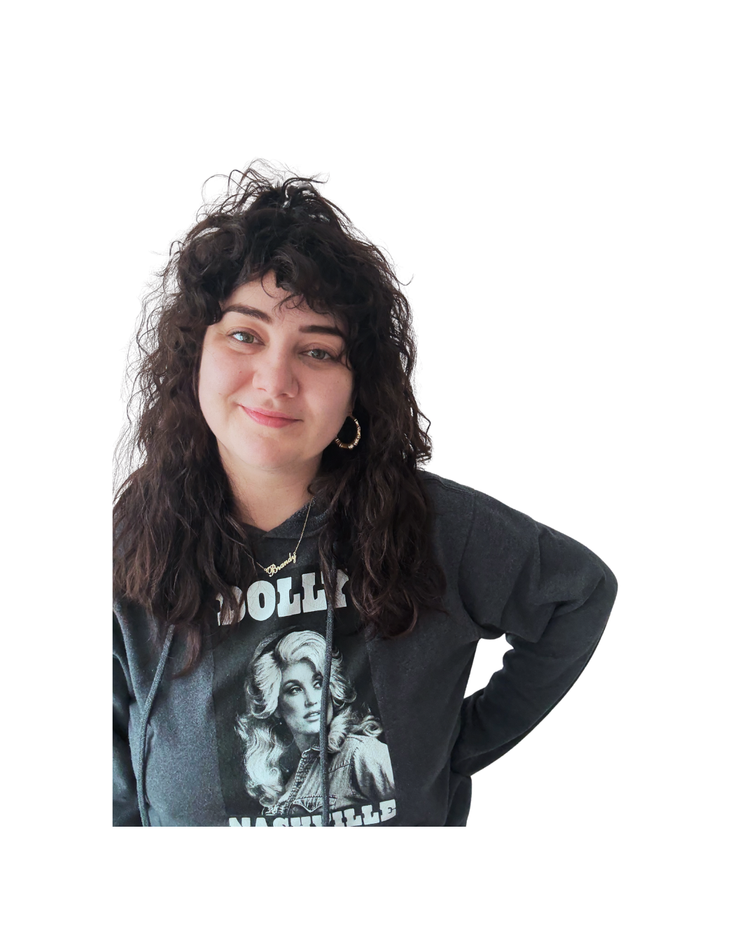 Young woman with curly dark hair, wearing gold hoop earrings, a dolly parton hoodie, posing with a slight smile.