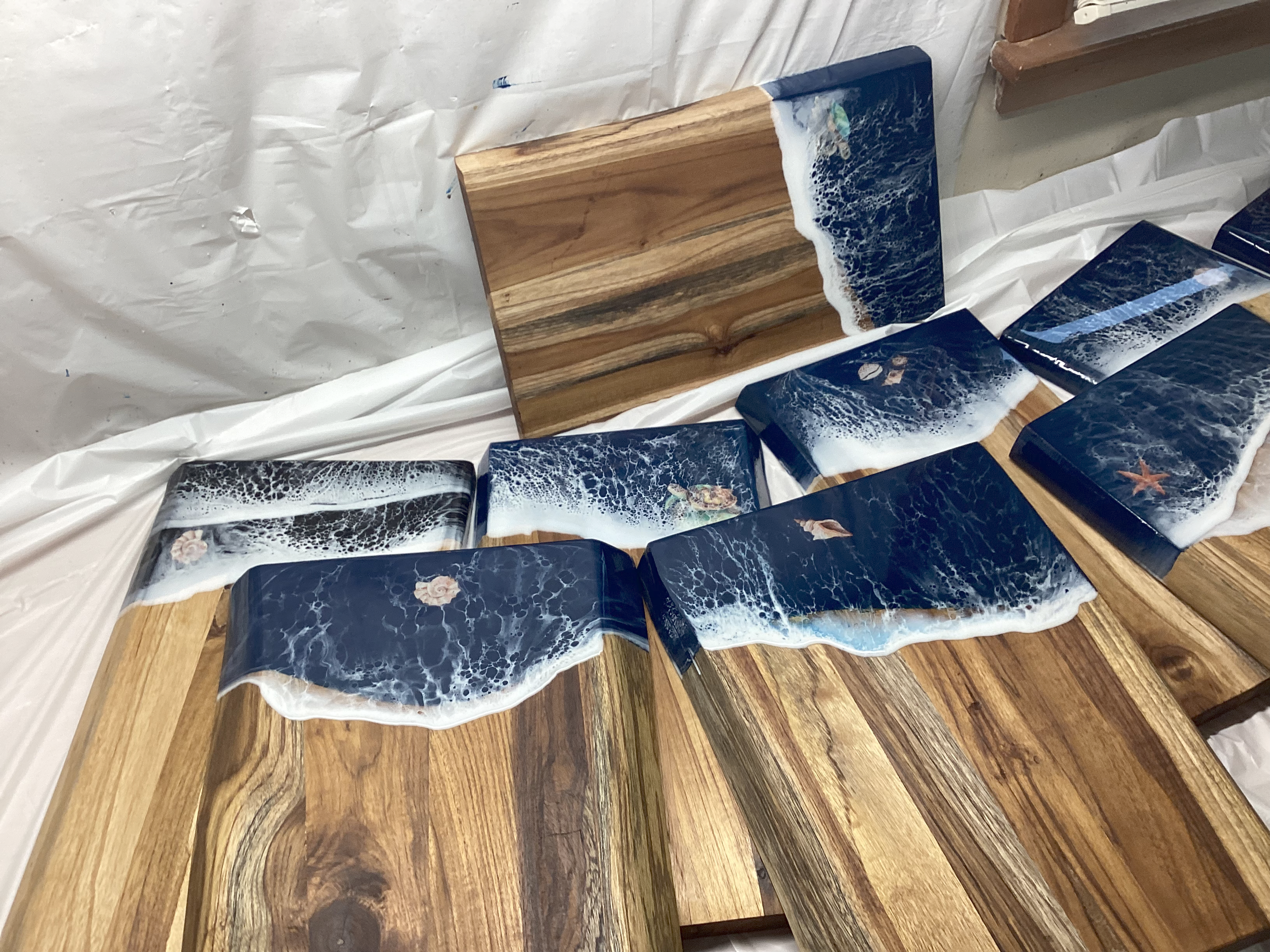 Multiple wooden boards with ocean wave designs and sea creature illustrations on their surfaces, arranged on a white plastic-covered surface.