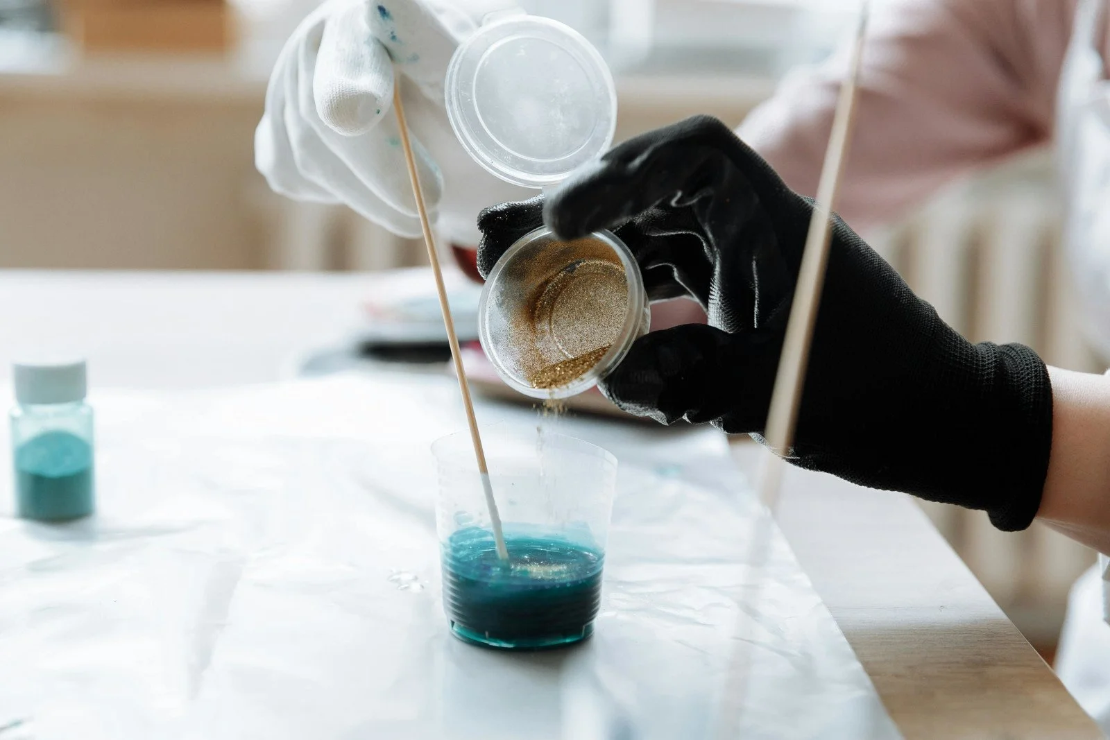 Artist mixing blue and gold resin pigments during the creative process at Stark Art.