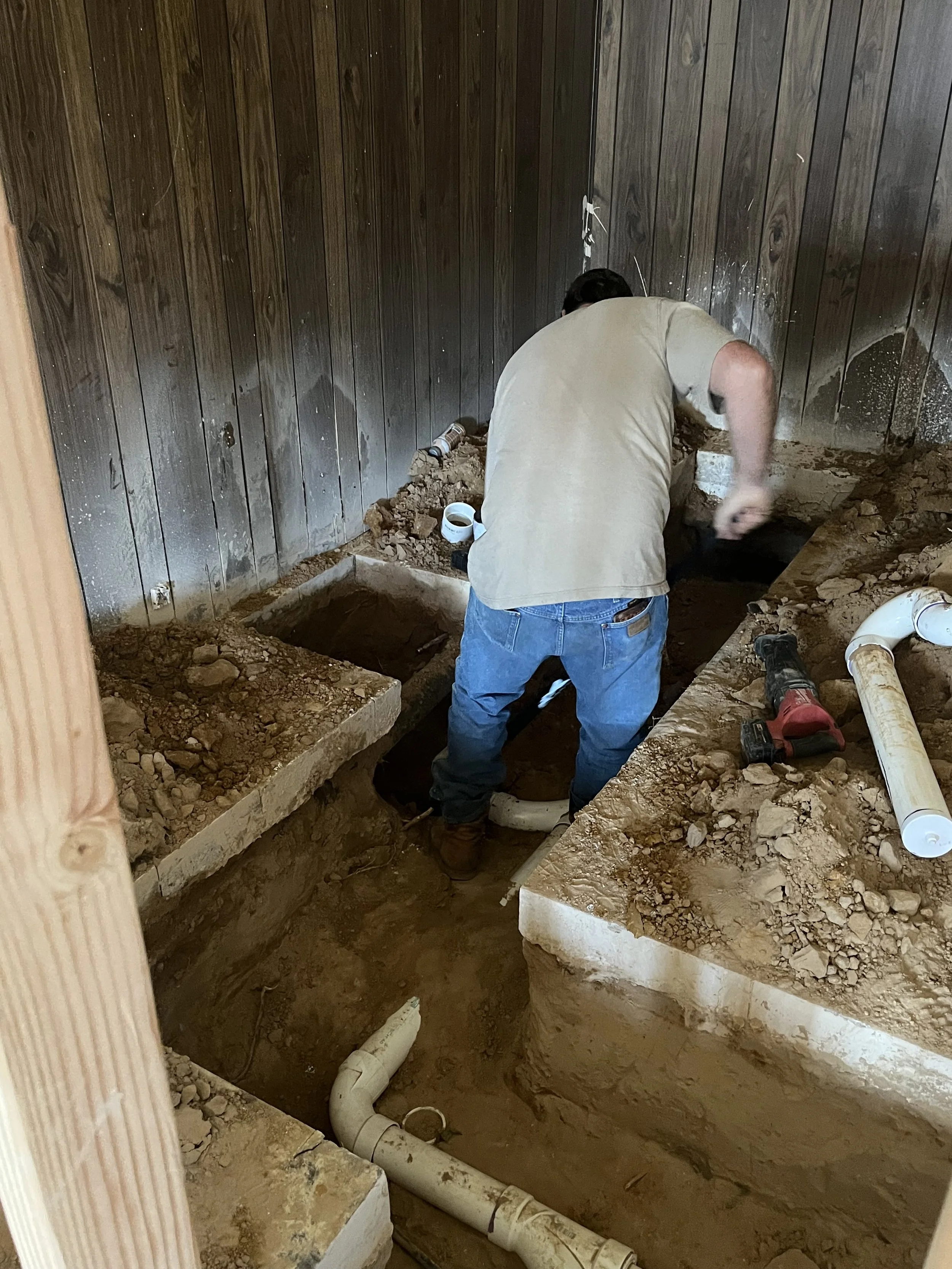 A man working in a room with exposed plumbing and wooden walls, installing or repairing pipes and fixtures.