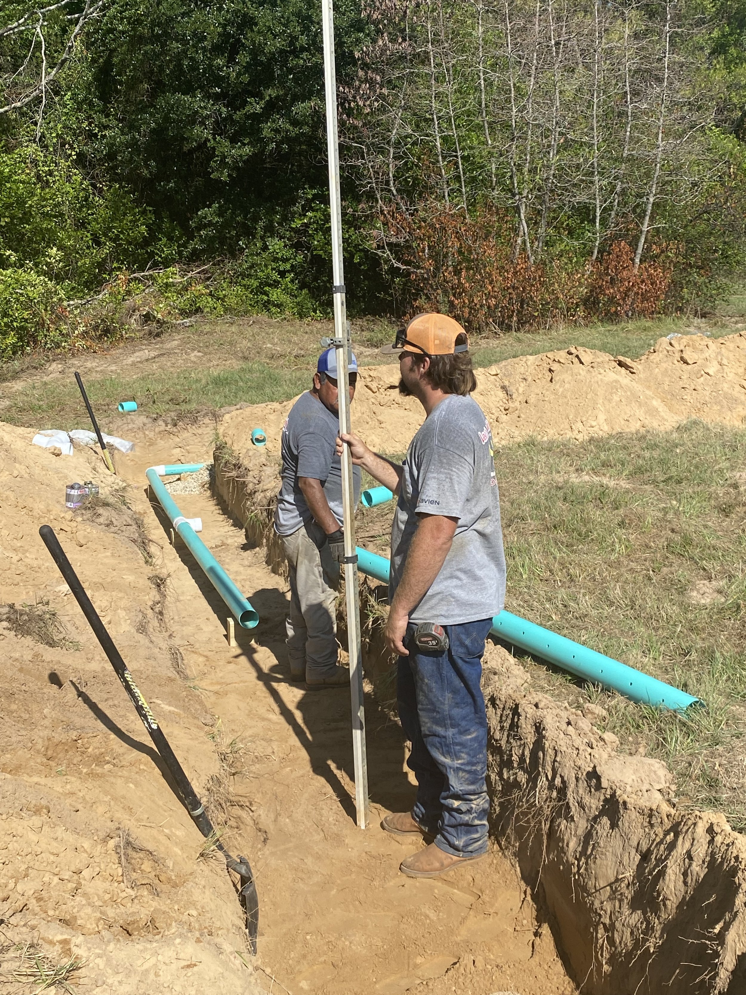 Two construction workers install or repair underground piping in a trench.