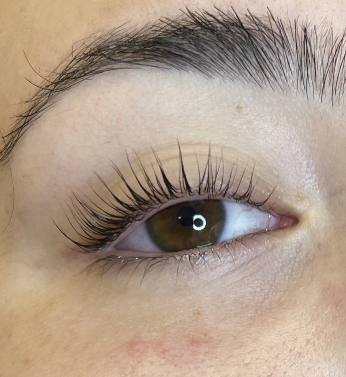 Waxer performing a brazilian wax on a woman laying down wearing an orange bikini bottom