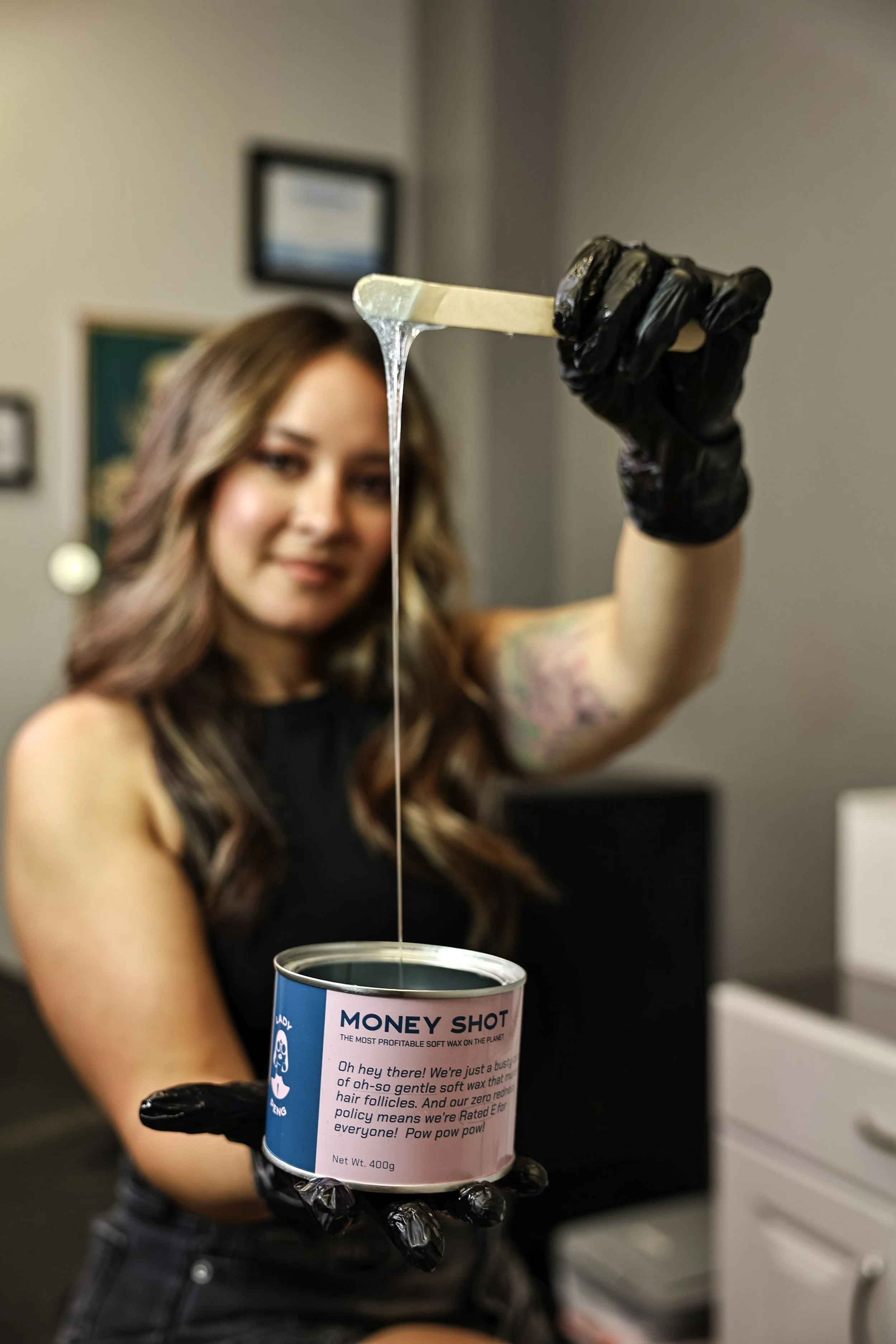 Esthetician holding a waxing stick above an open can of soft wax, showing the texture and consistency.