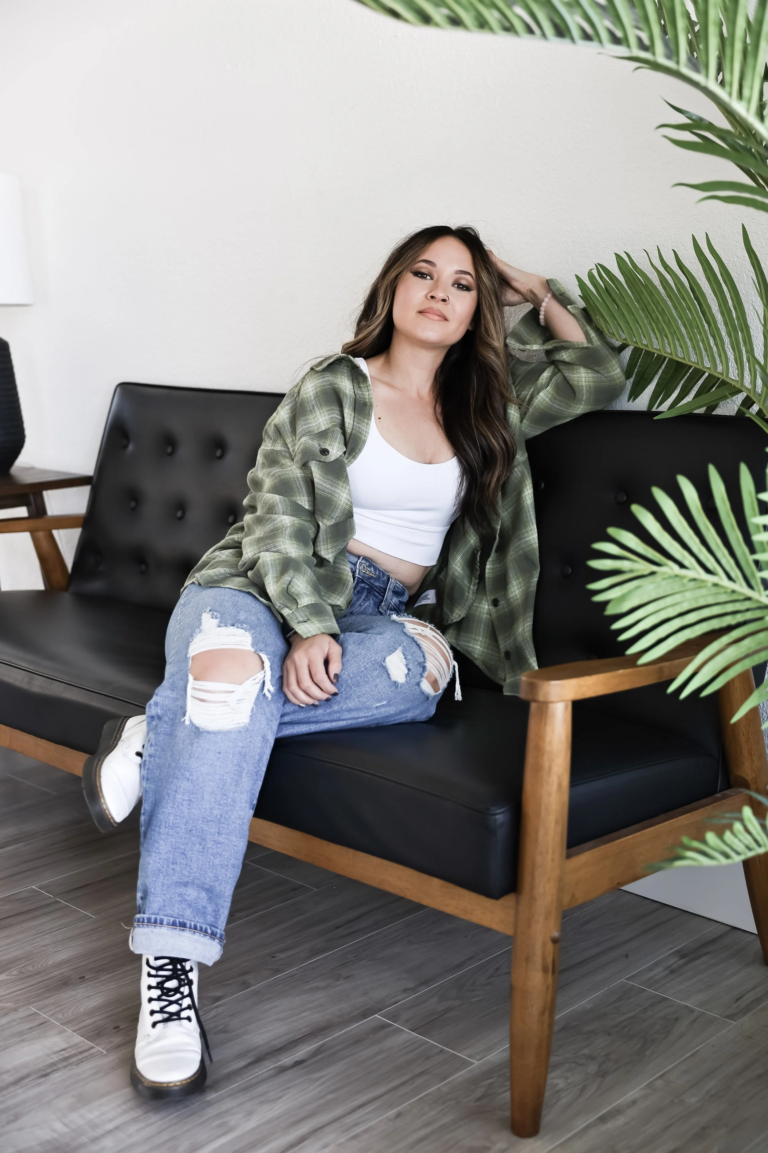 Jackie relaxing on a black leather couch in a modern studio, framed by green plants.