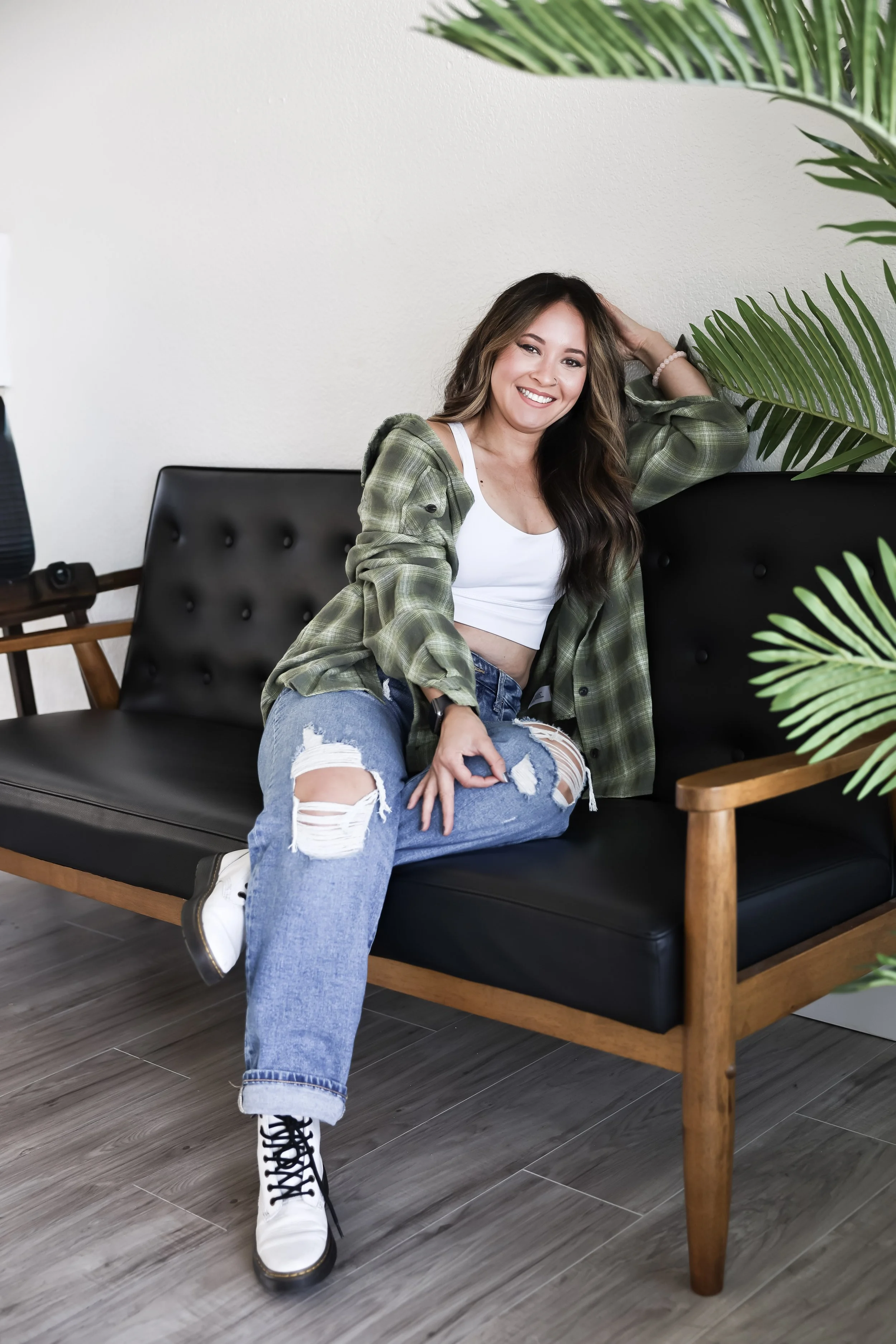 Jackie relaxing on a black leather couch in a modern studio, framed by green plants.