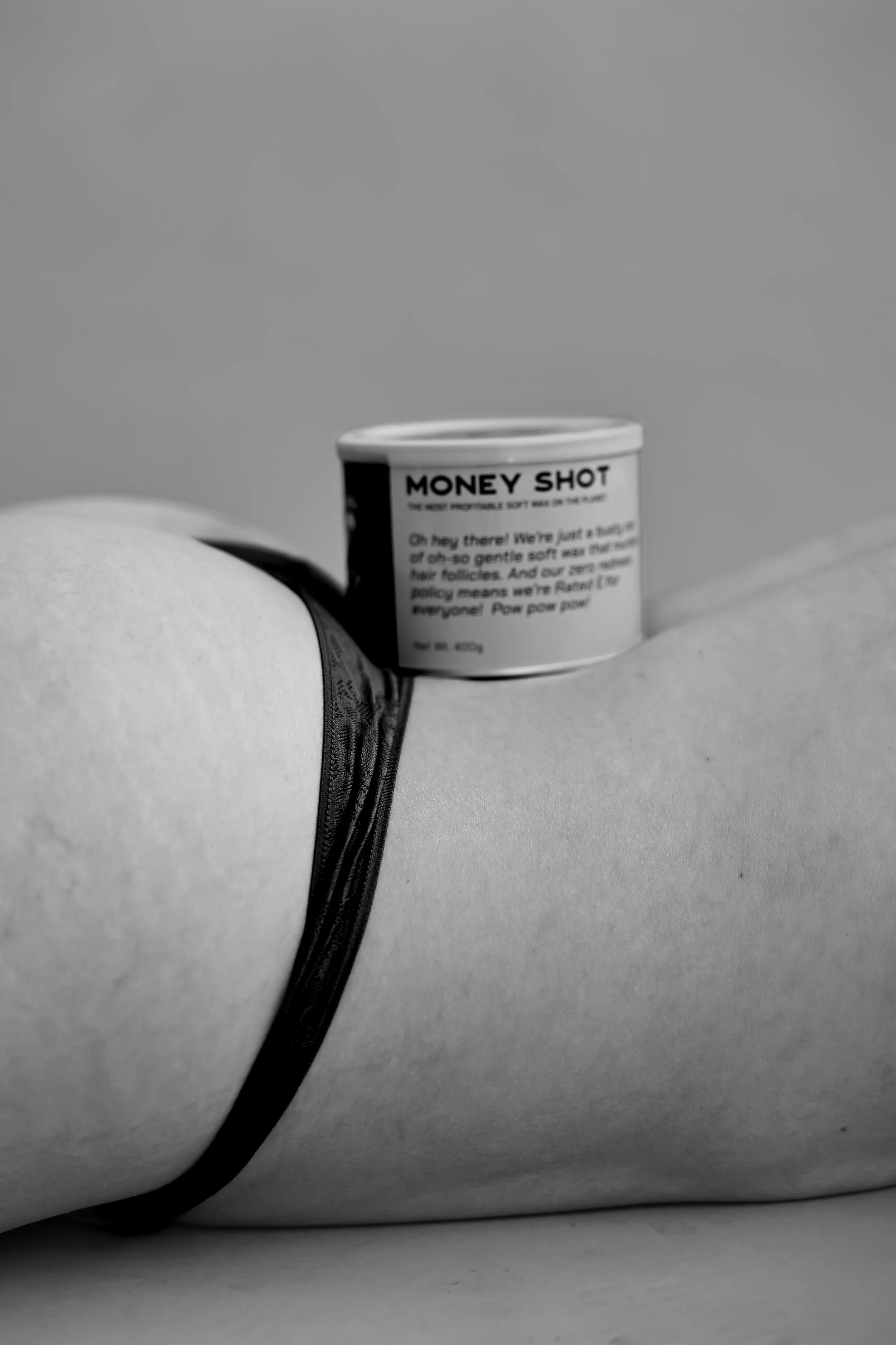 Black and white close-up of a waxing product can resting on a client’s lower back during a studio photoshoot.
