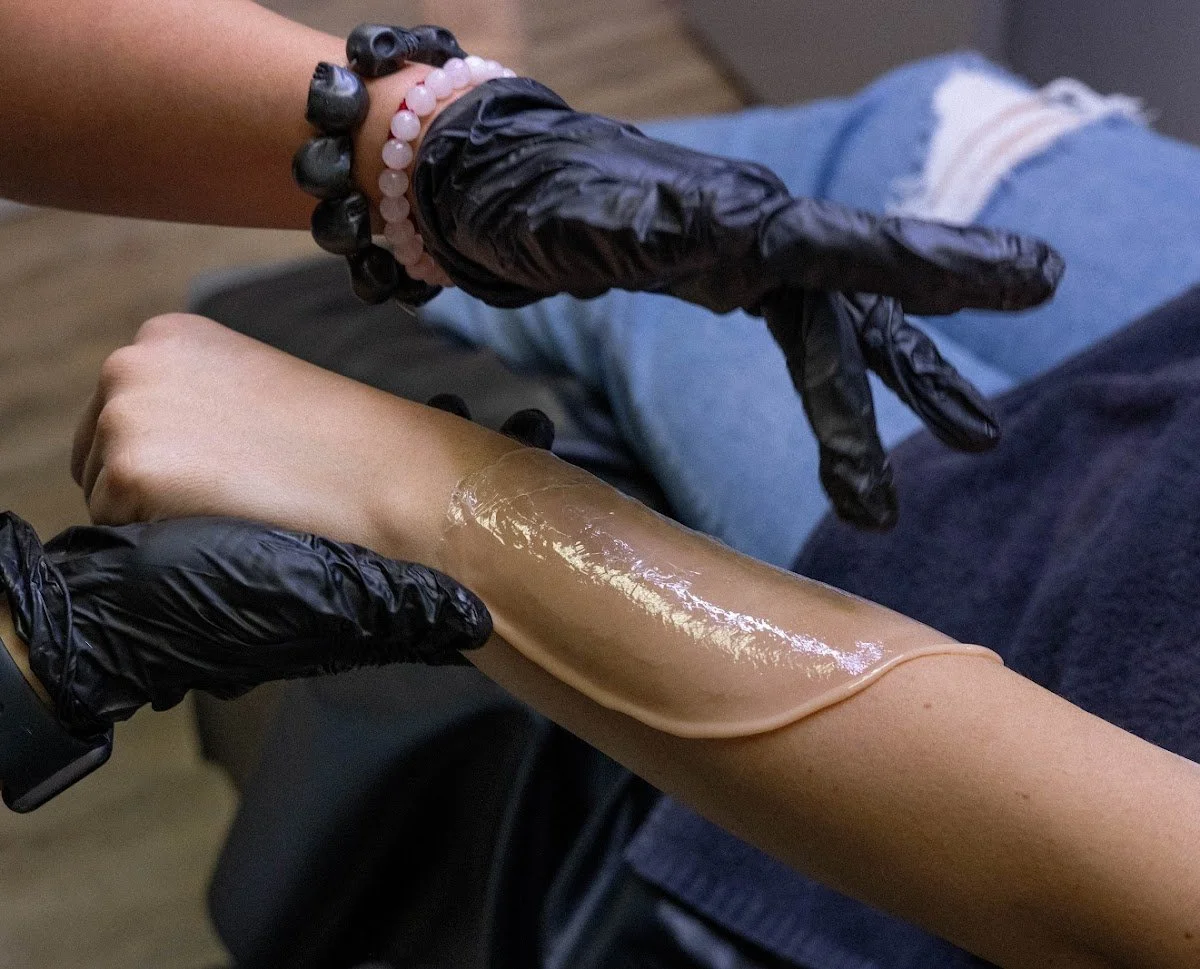 Esthetician removing a strip of hardened soft wax from a client’s forearm during a waxing treatment.