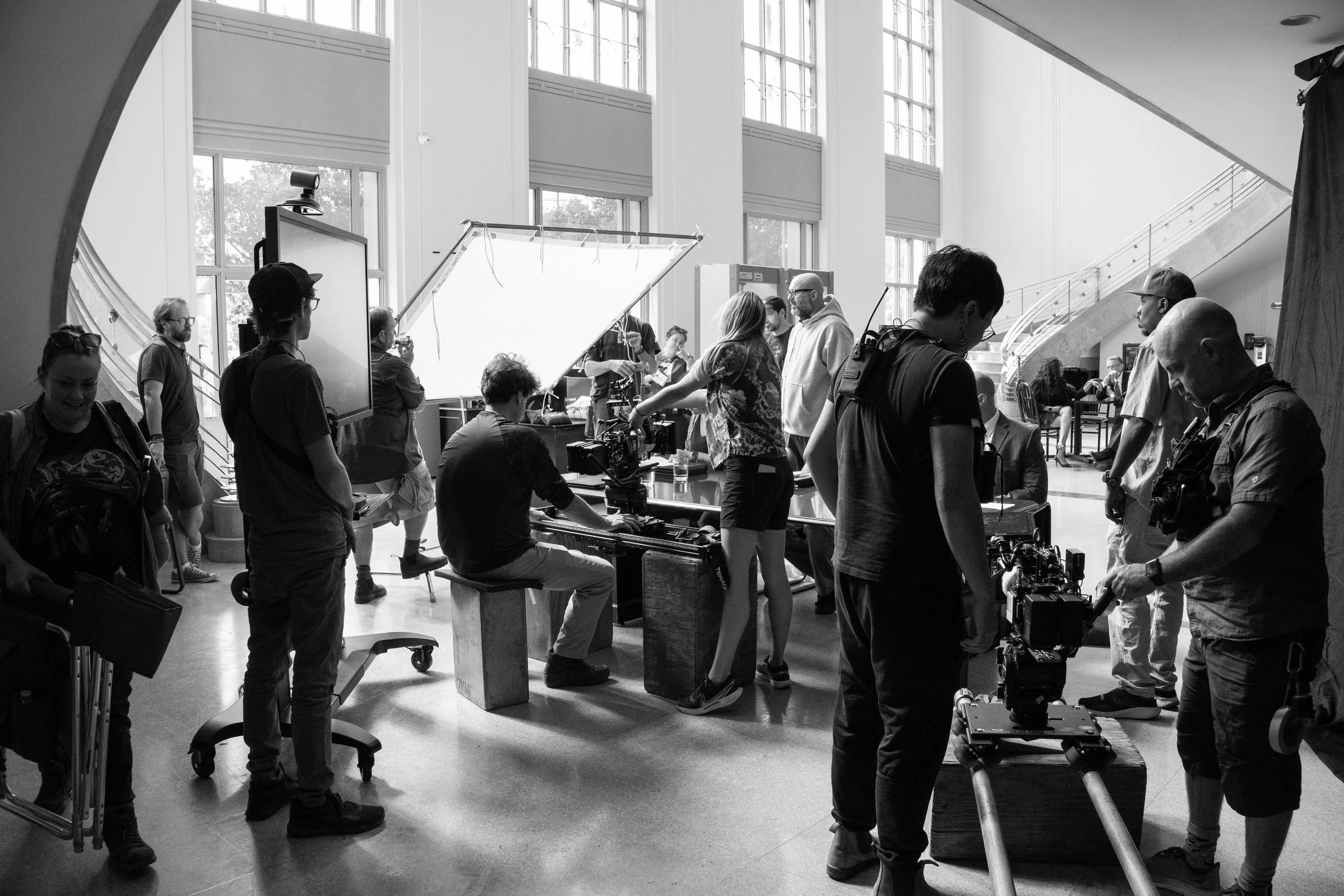 Filmmaking crew working on a set inside a well-lit building with large windows.