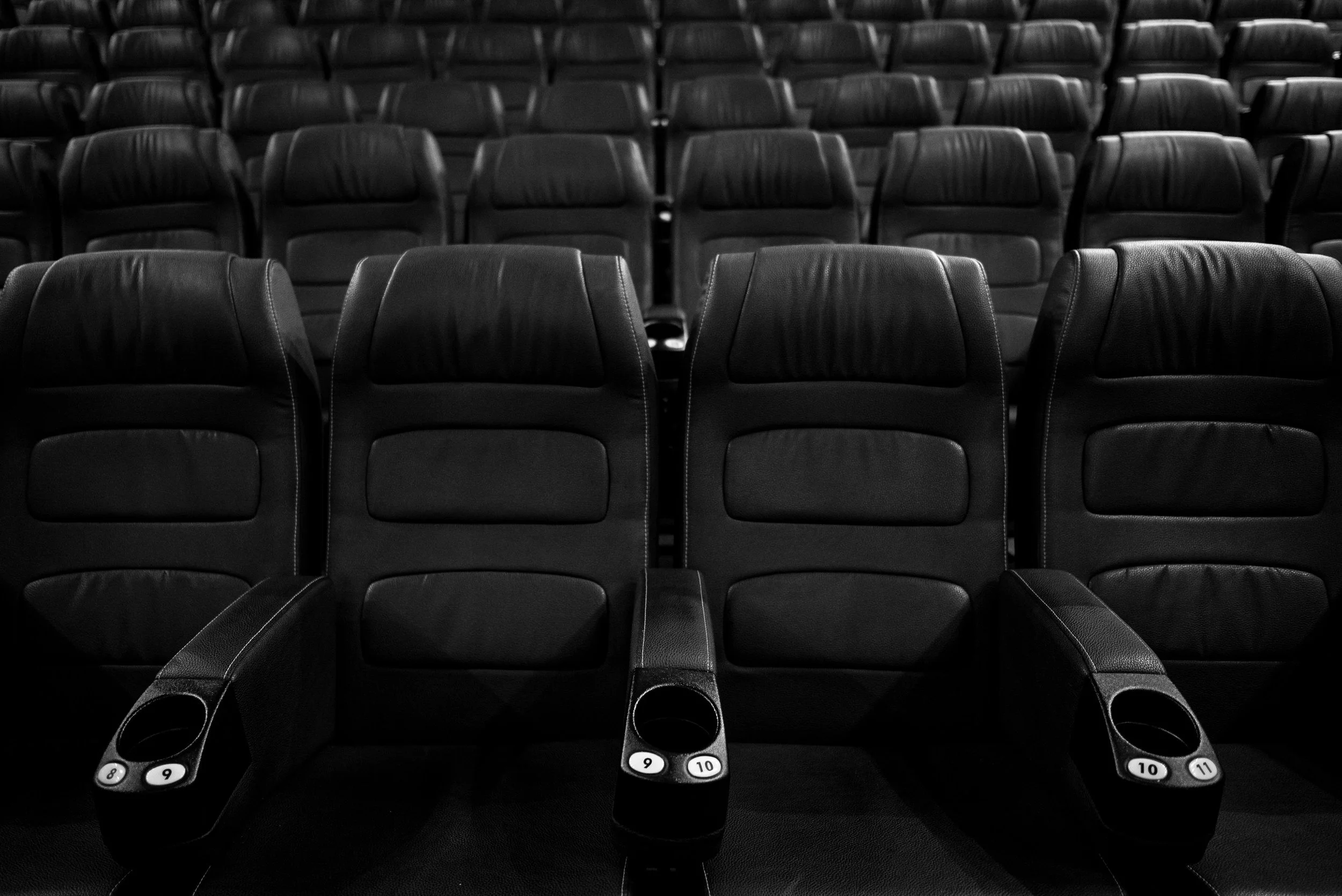 Empty black theater seats with numbered cup holders in a darkened auditorium.