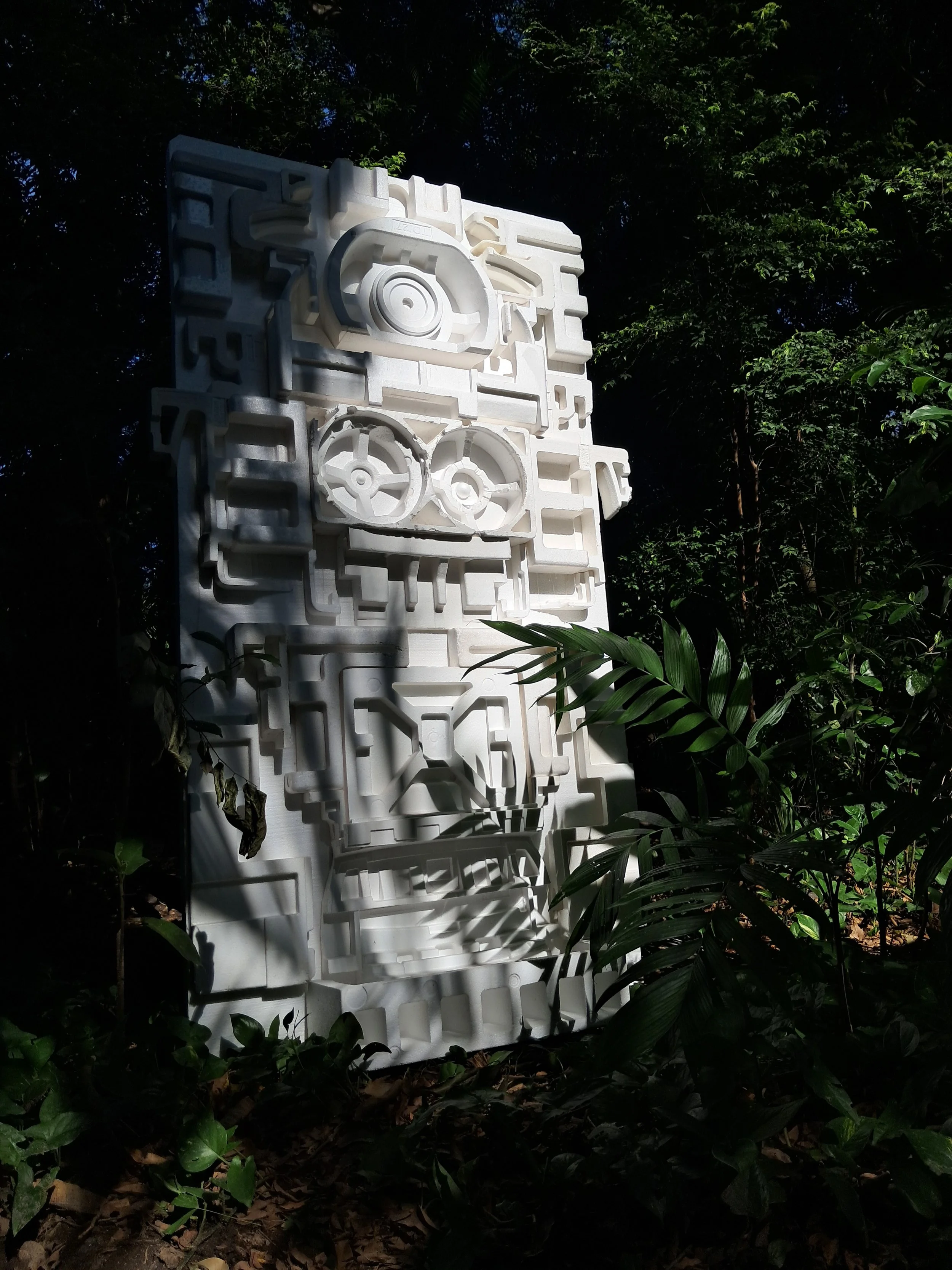 Estructura de espuma blanca en medio de un jardín con árboles y plantas, con sombras y luz natural.
