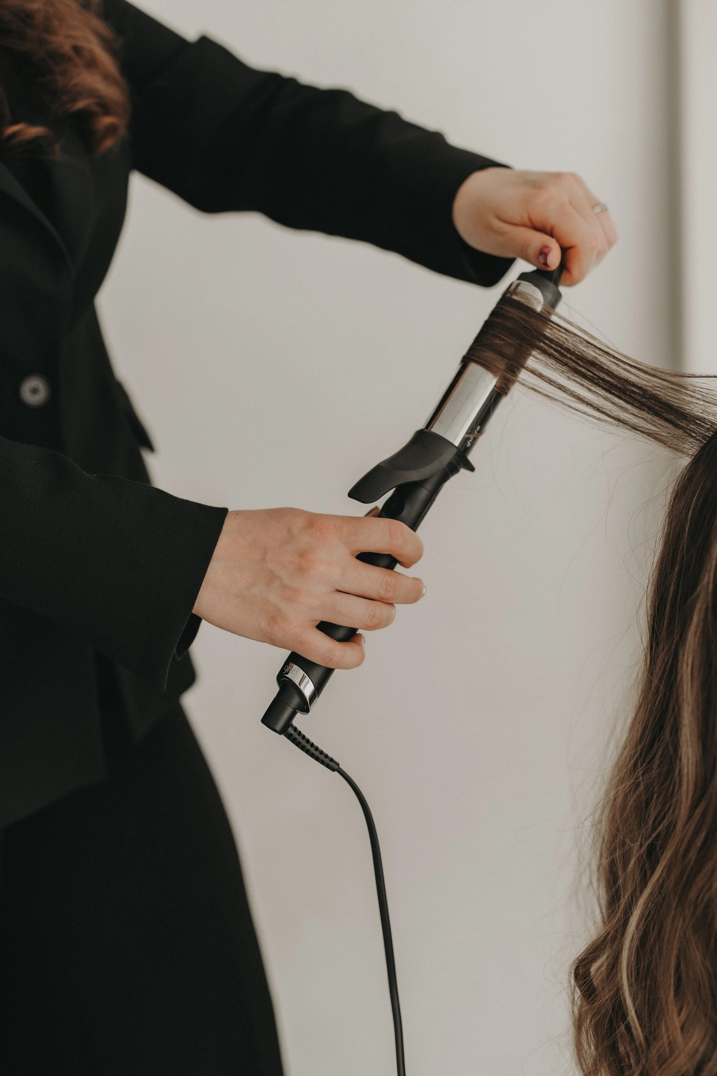 Une personne utilise un fer à lisser pour coiffer des cheveux longs et bruns.