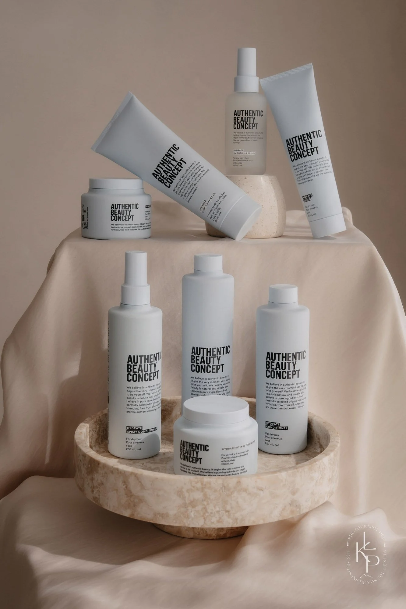 Gamme de produits de soins capillaires de la marque Authentic Beauty Concept, disposés sur une table en pierre beige avec un fond neutre.