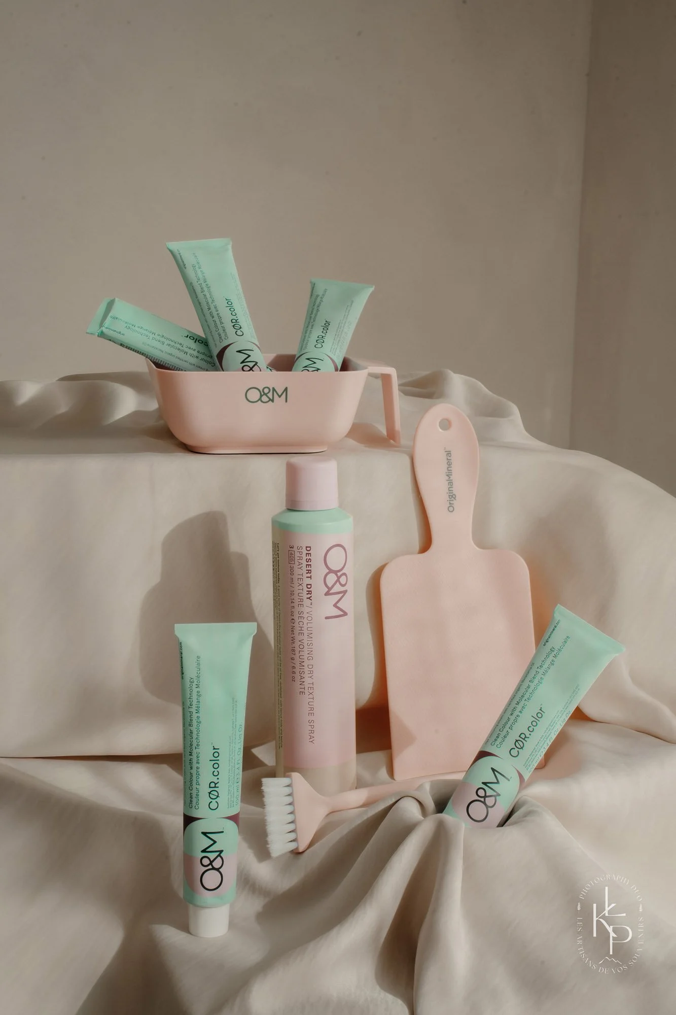 Une collection de produits de soins et accessoires en couleurs pastel, comprenant une brosse à dents et des tubes de dentifrice, disposés de manière esthétique sur un tissu beige.