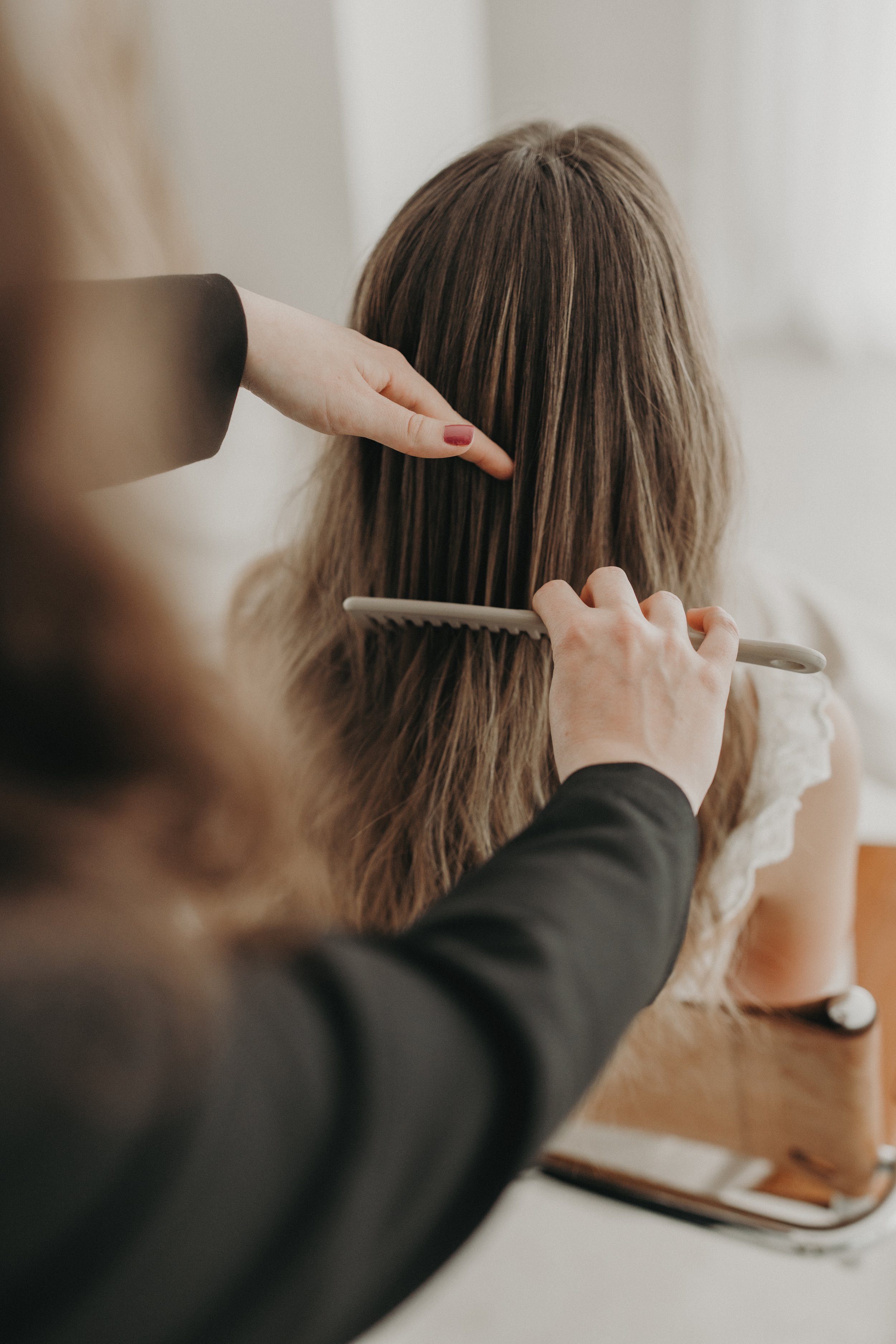 Une personne en train de coiffer les cheveux d'une autre personne assise, avec un pinceau à cheveux dans la main et une main qui tient la tête.