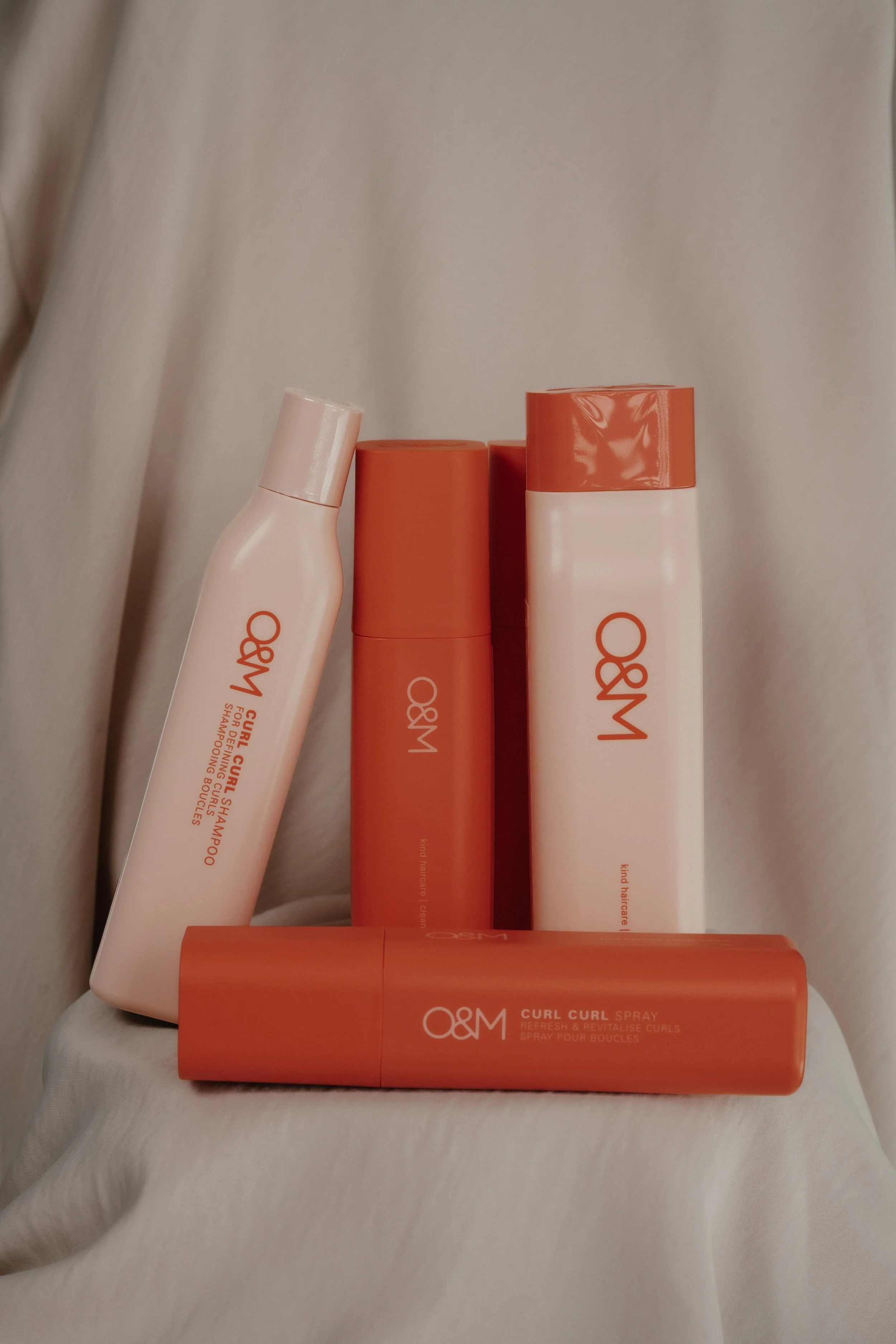 Gamme de produits capillaires orange et blanc, comprenant un spray et des bouteilles, sur un fond neutre beige.