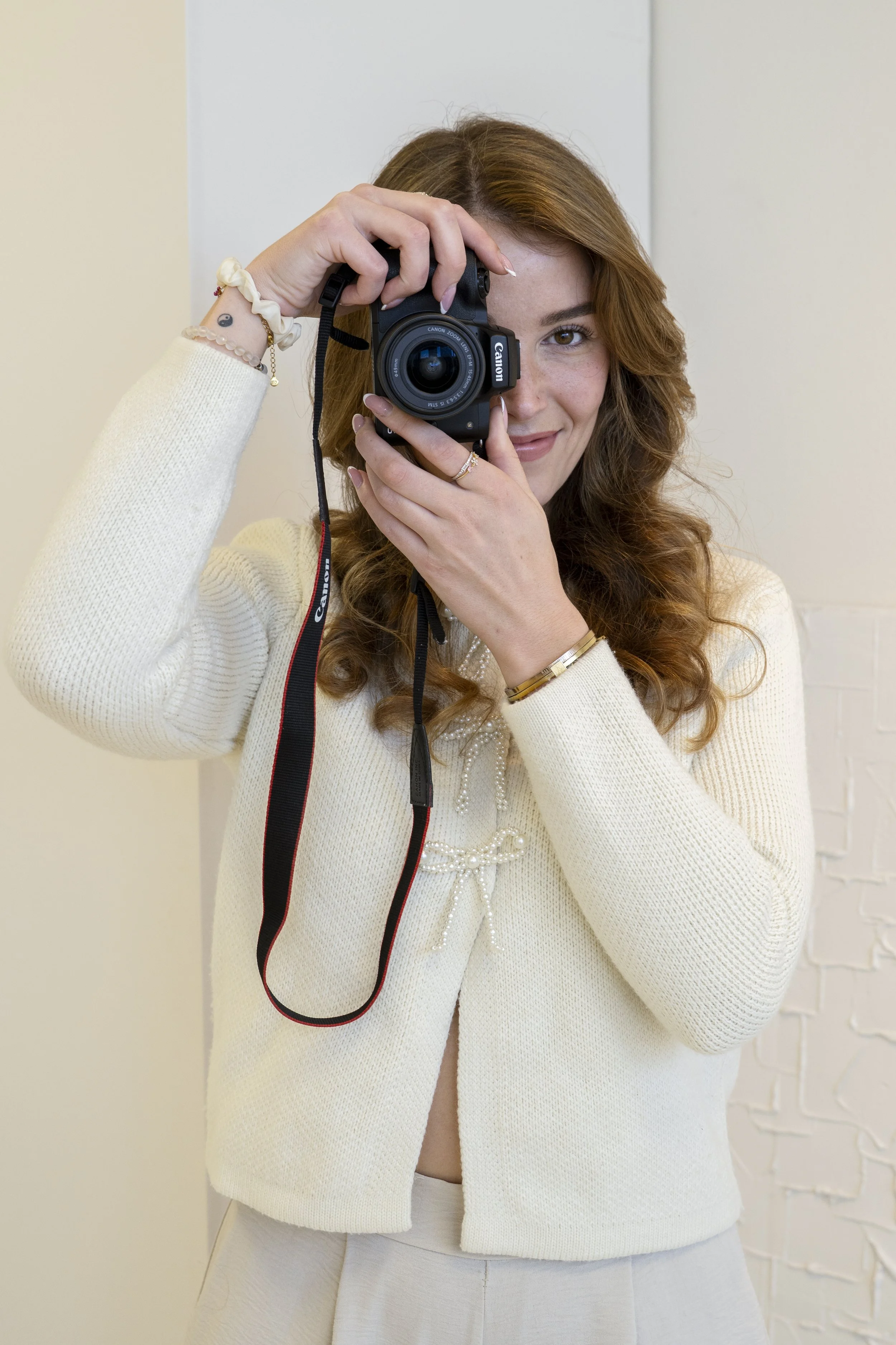 Vrouw houdt een Canon camera vast en neemt een foto, met een witte blazer en een lach.