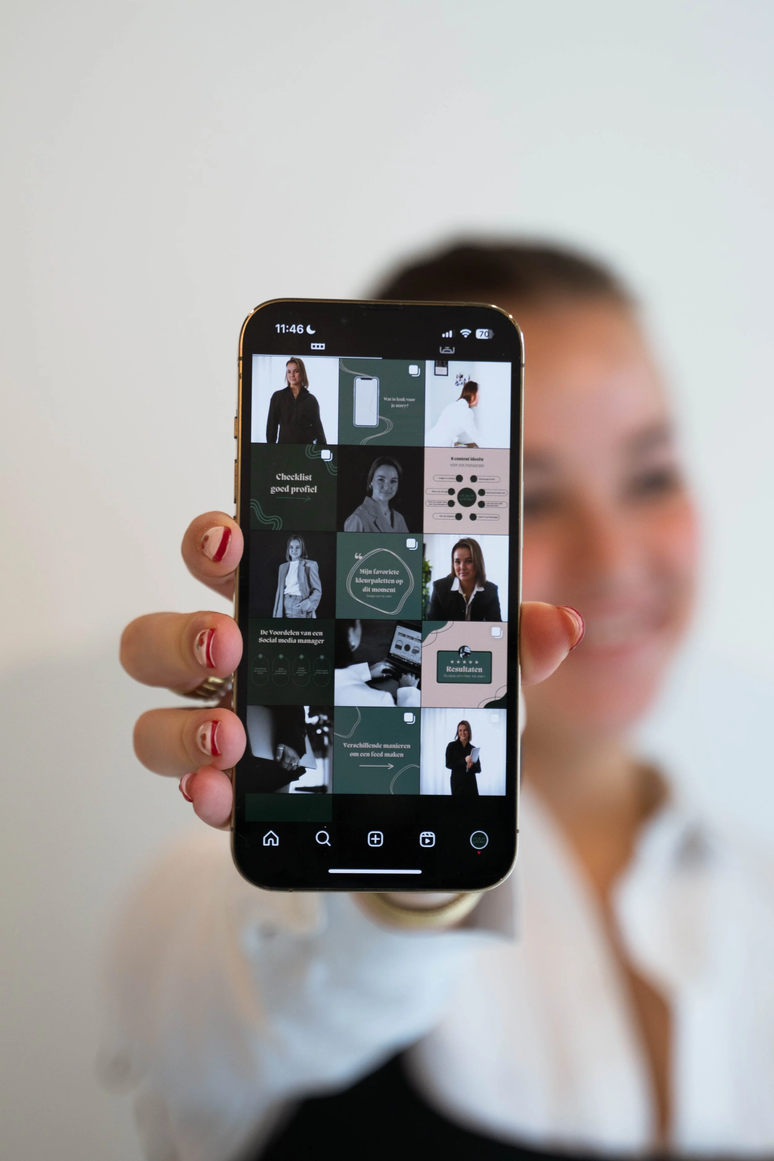 Persoon houdt een smartphone voor zich vast met op het scherm een collage van zakelijke social media berichten, terwijl ze in de achtergrond uitgestoken hand en een wit shirt heeft.