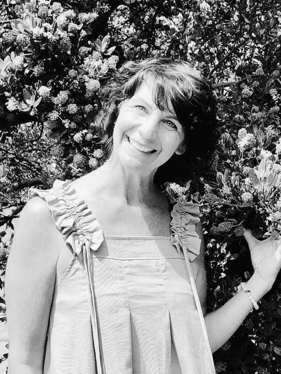 A woman smiling outdoors with flowers in the background.
