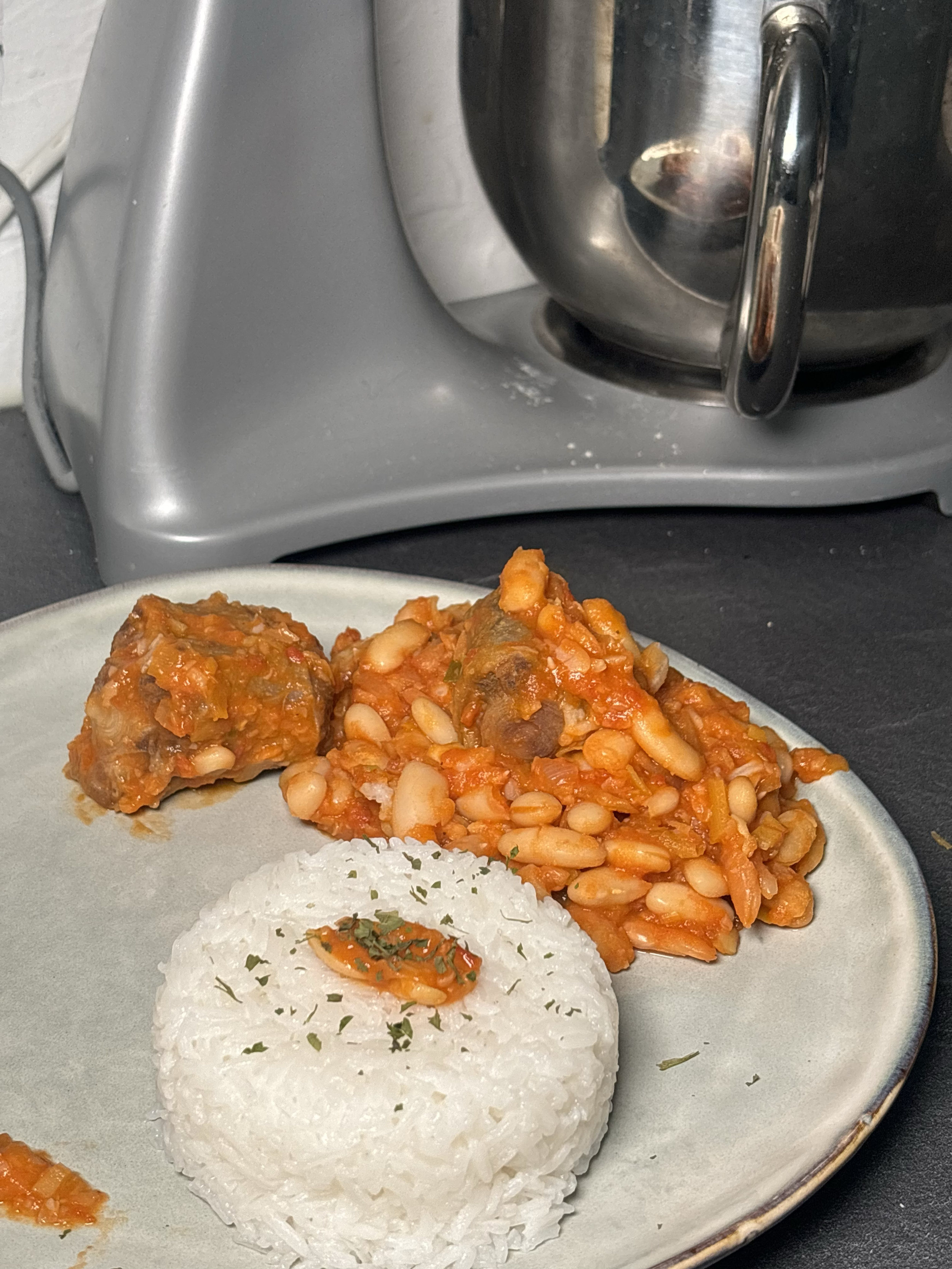 Assiette de riz blanc avec un peu de garniture, accompagnée de boulettes de viande en sauce avec des haricots et des légumes.