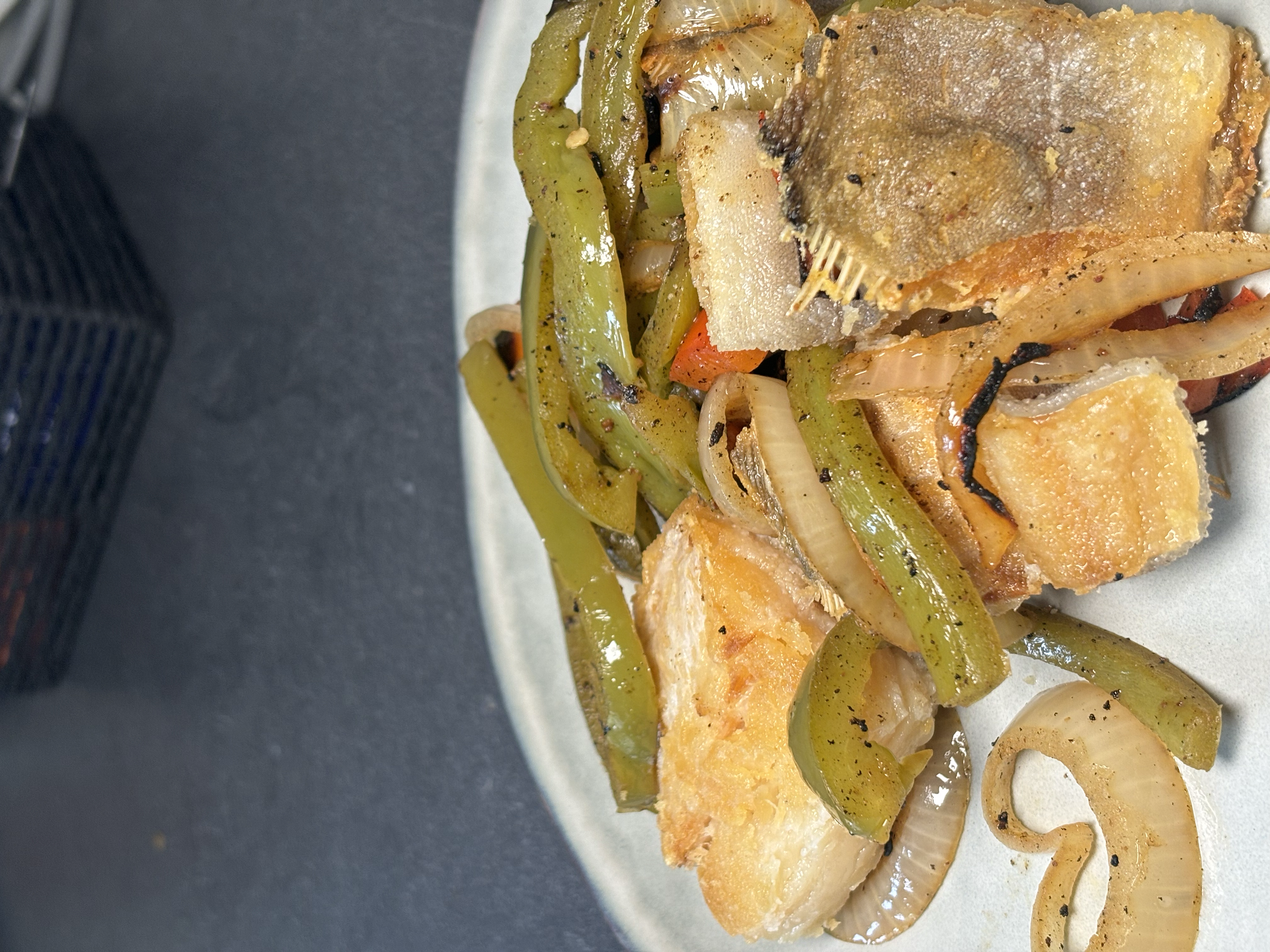 Poisson frit avec légumes sautés, comprenant des oignons et des poivrons verts.