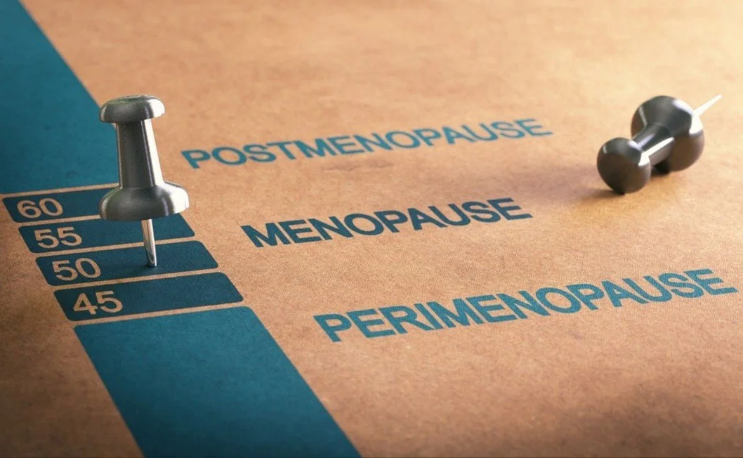 A game board with a blue section indicating different phases of menopause: premenopause, perimenopause, menopause, and postmenopause. Two pushpins are on the board, one on the menopause stage and one on perimenopause, with a small black dumbbell-like object nearby.