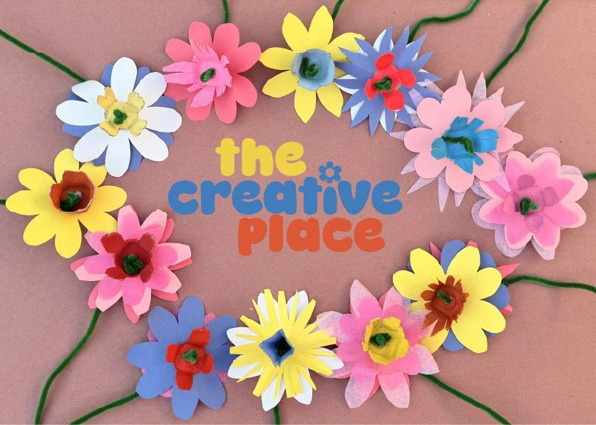Colorful paper flowers arranged in a circle around the words 'the creative place' on a pink background.