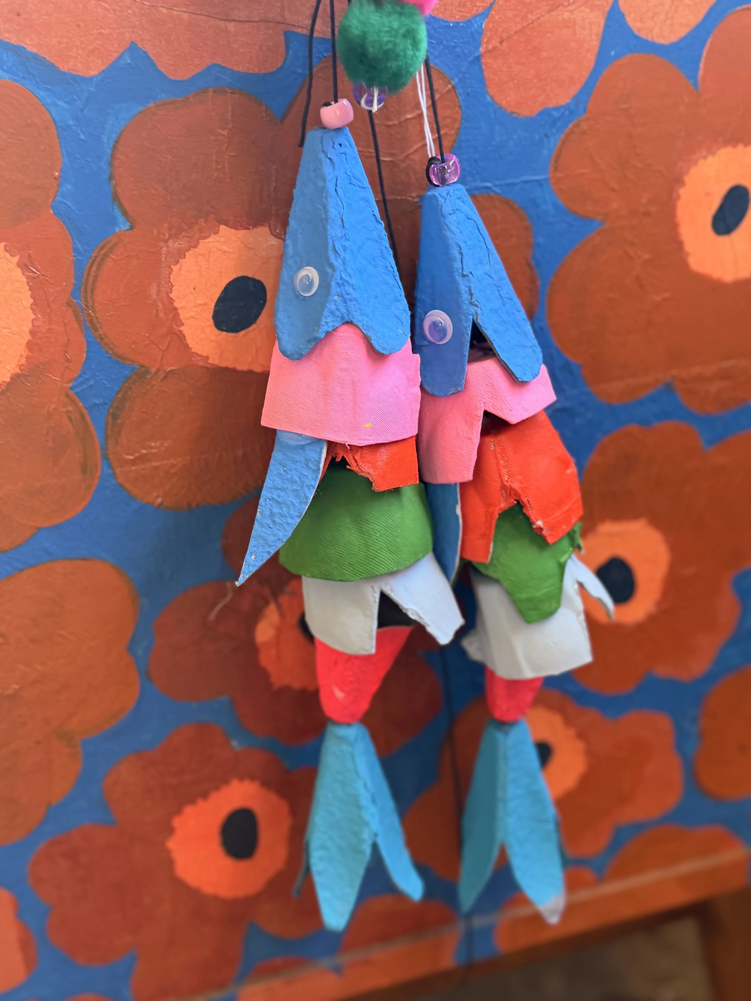 Colorful handmade fish-shaped fabric ornaments hanging against a floral patterned background.
