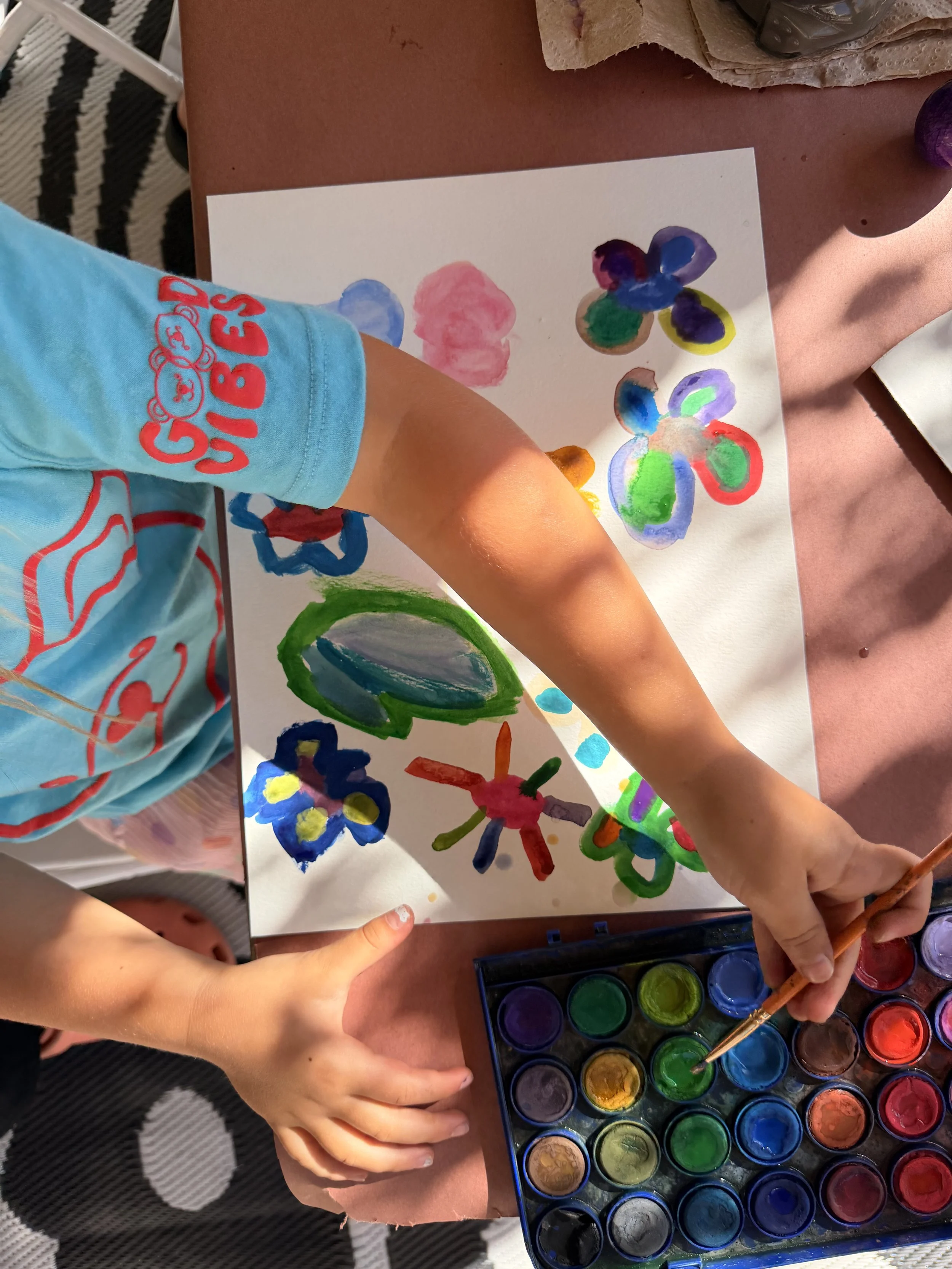 Child creating colorful watercolor paintings on paper using various shades of paint.