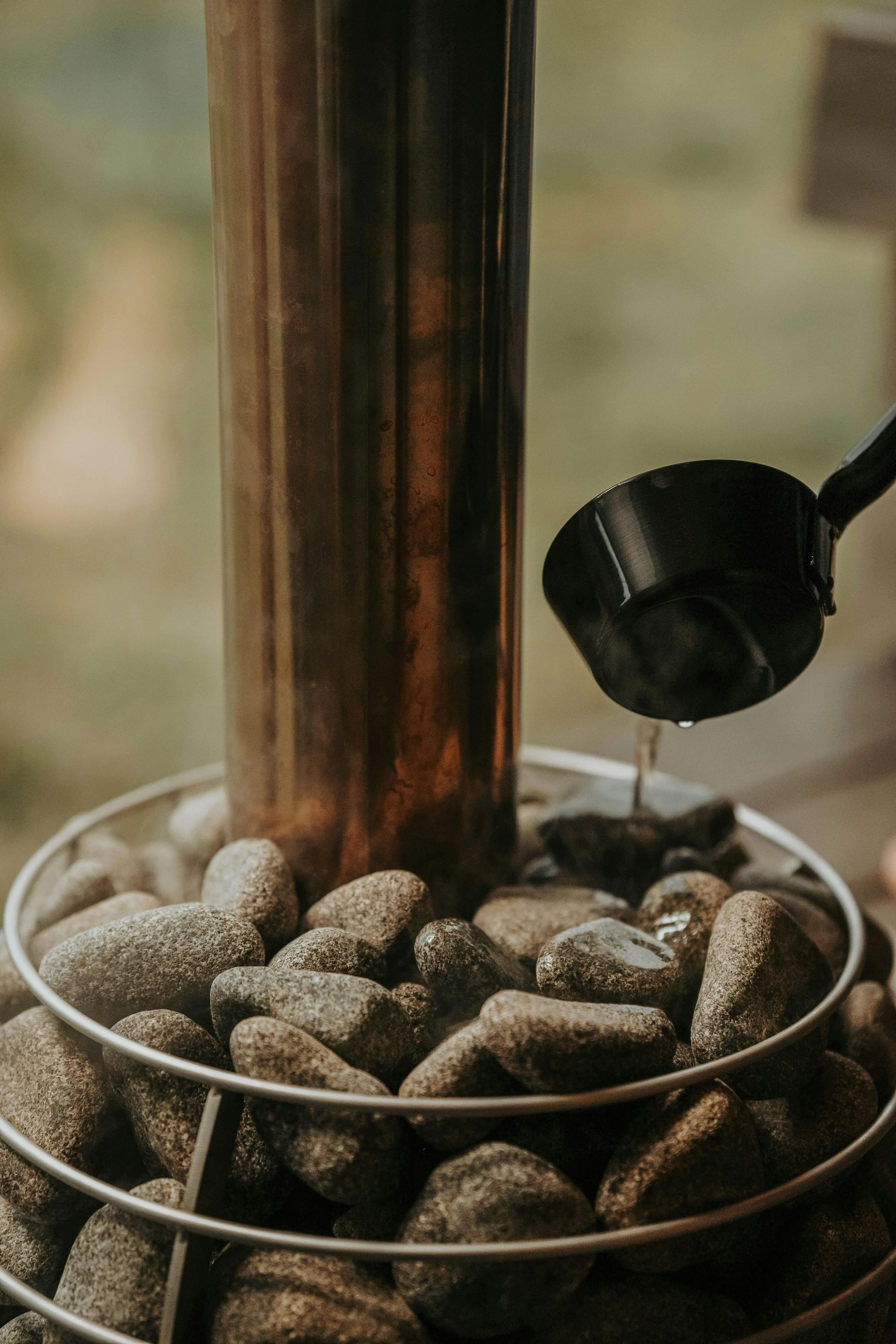 A metal water dispenser with a spout, surrounded by smooth gray stones, with water dripping from the spout.