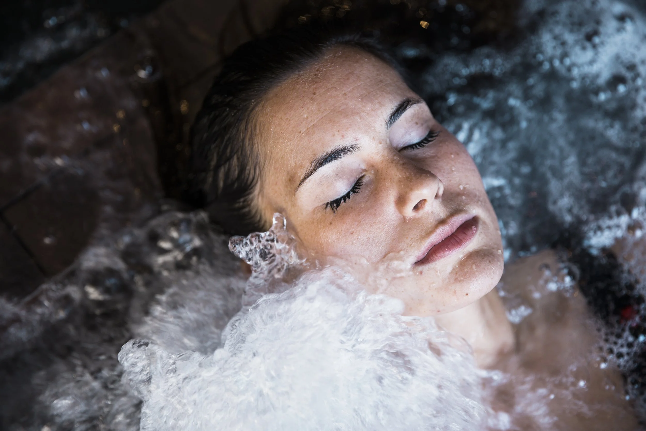 A woman with wet hair and closed eyes plunging into cold water.