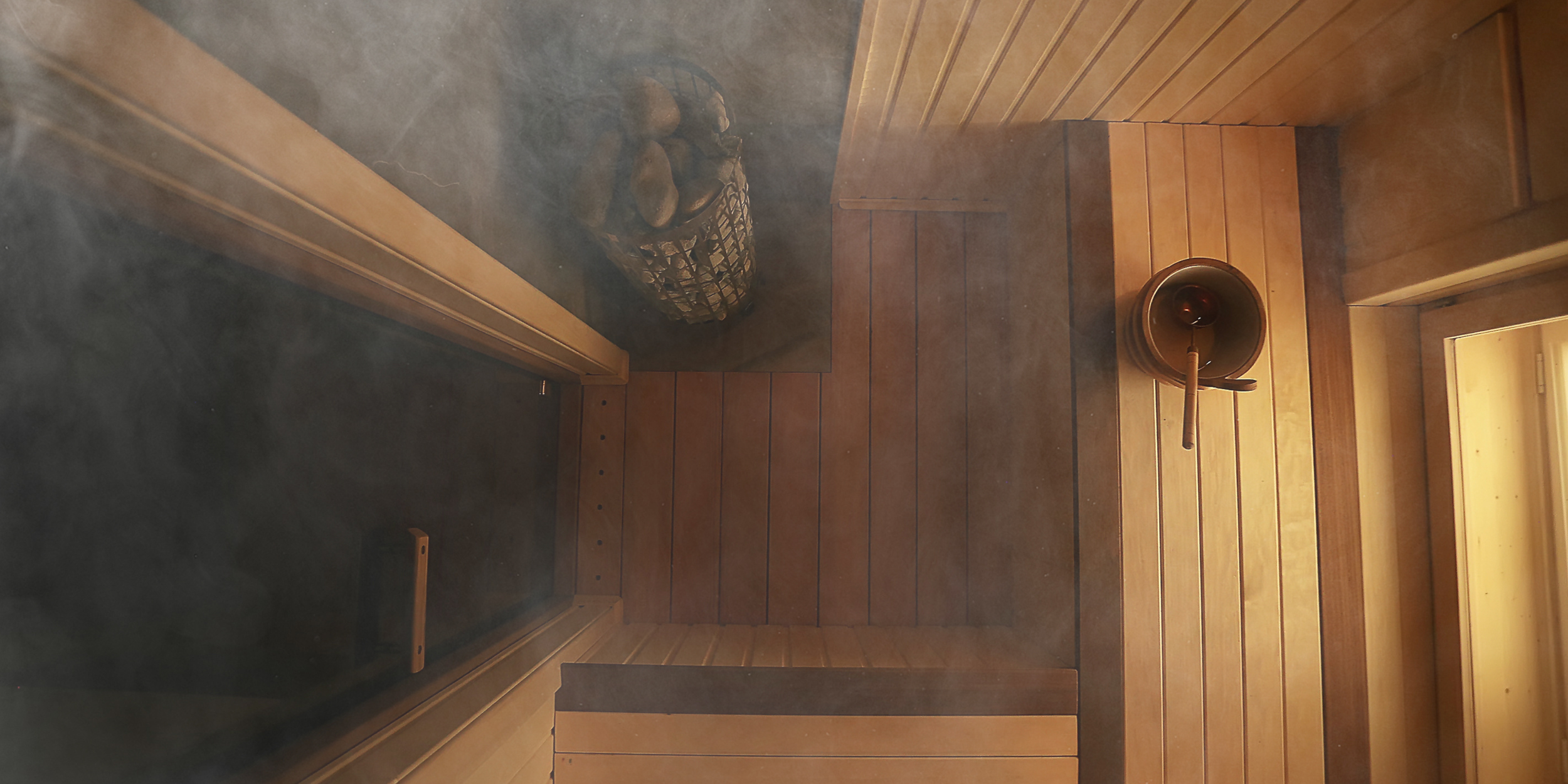 Interior of a traditional wooden sauna with a bucket and ladle, a stool with stones, and wooden paneling on the walls and floor.