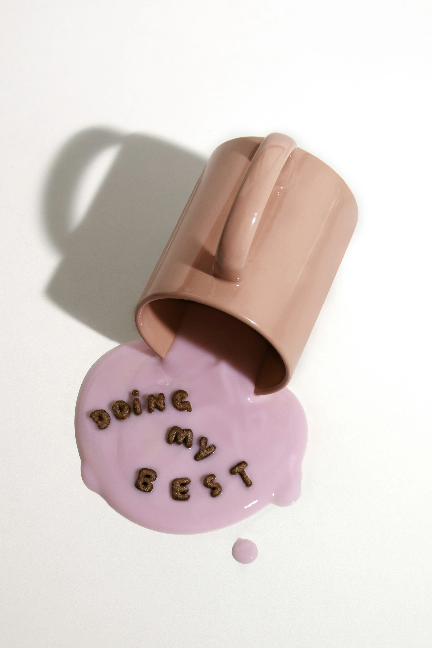 A mug spilling pink liquid with "doing my best" spelled out in chocolate cereal