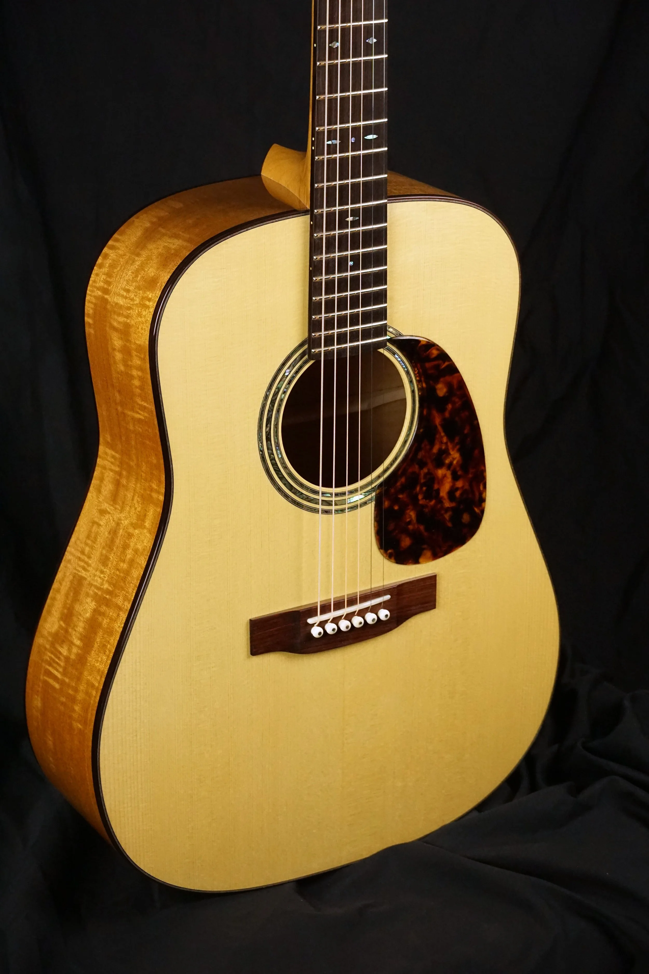 Steel string guitar with handmade pick guard on a black background.