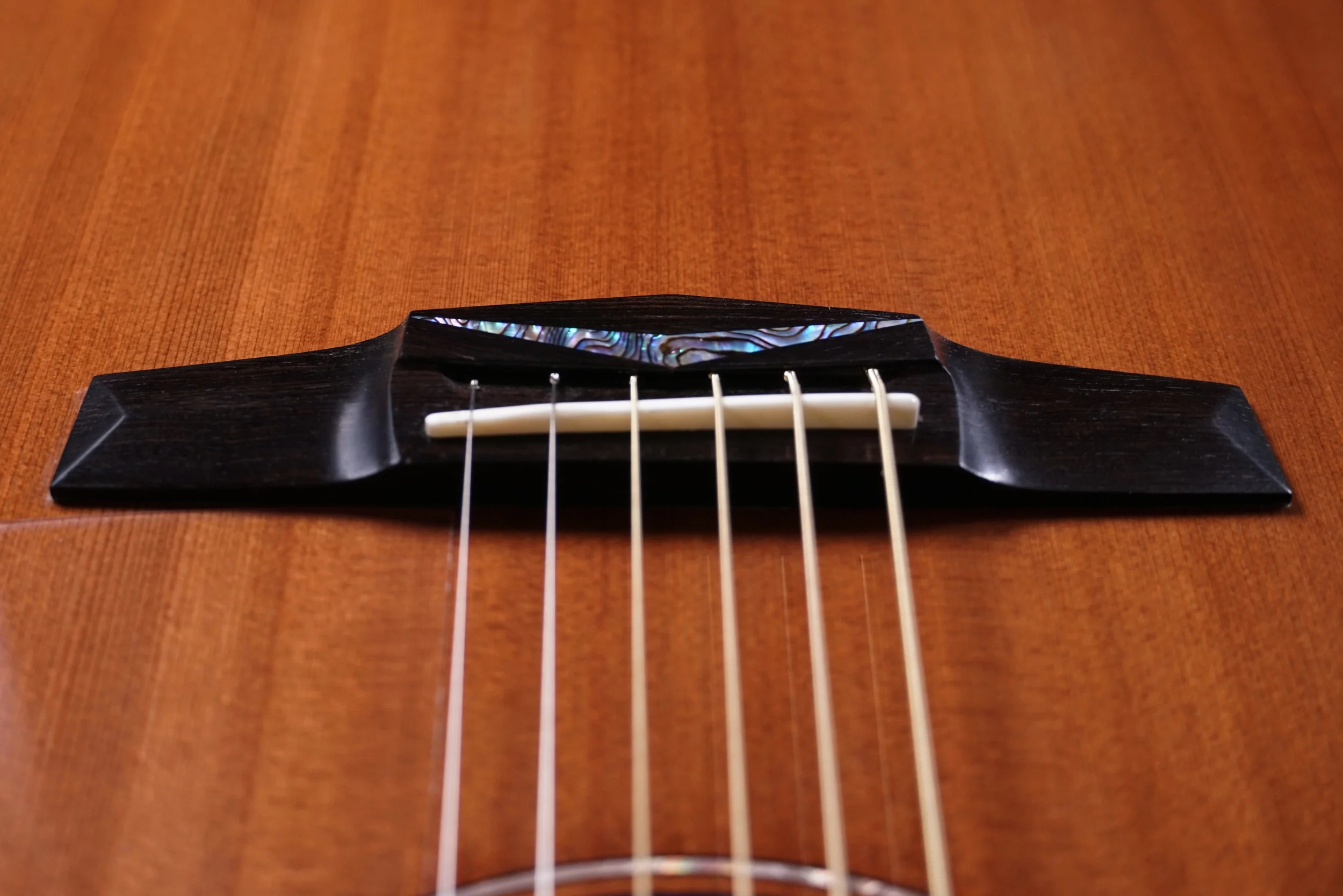 Close up of Pinless Stell Guitar Bridge with stone inlay on a redwood top.