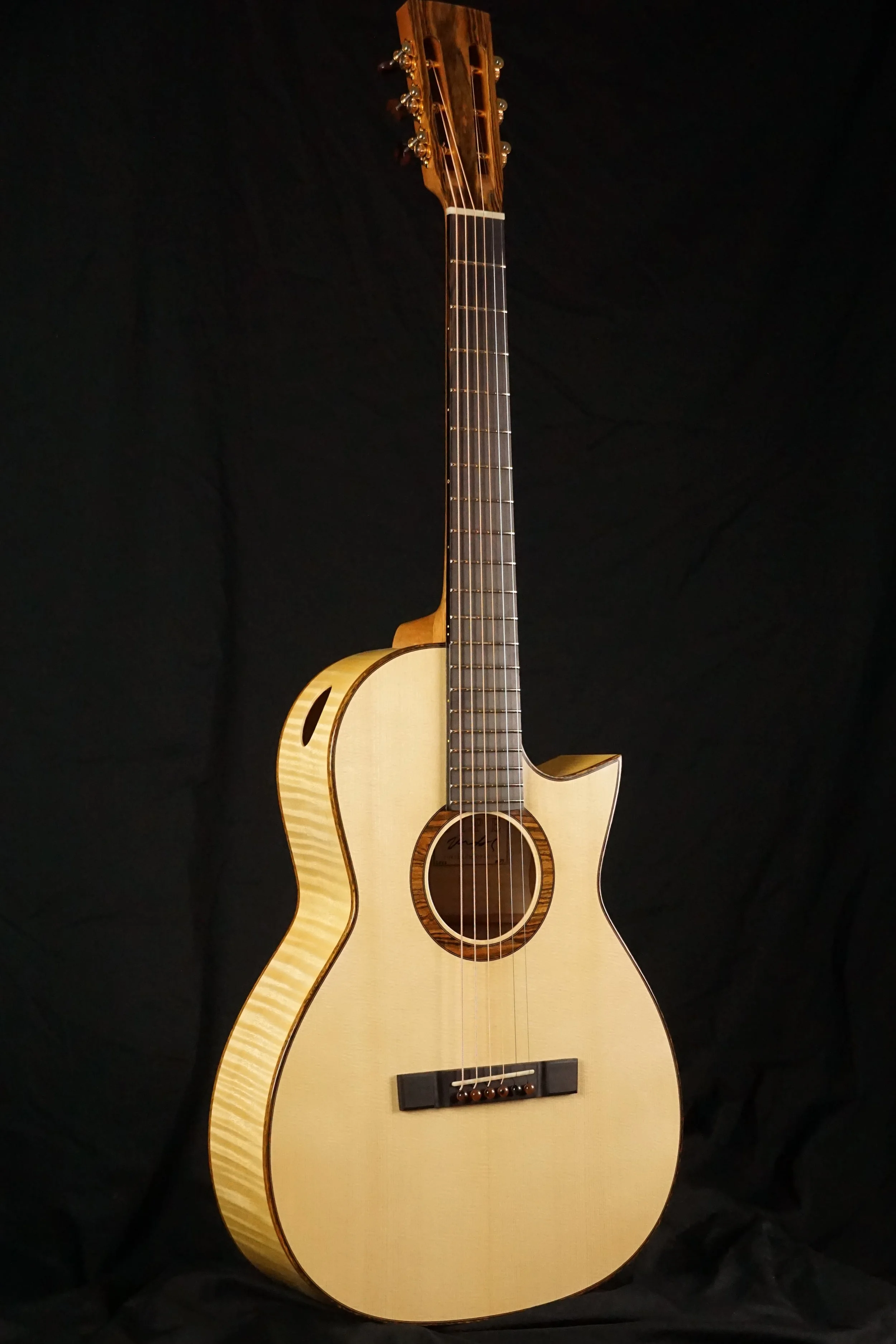 Maple steel string guitar on a black background.