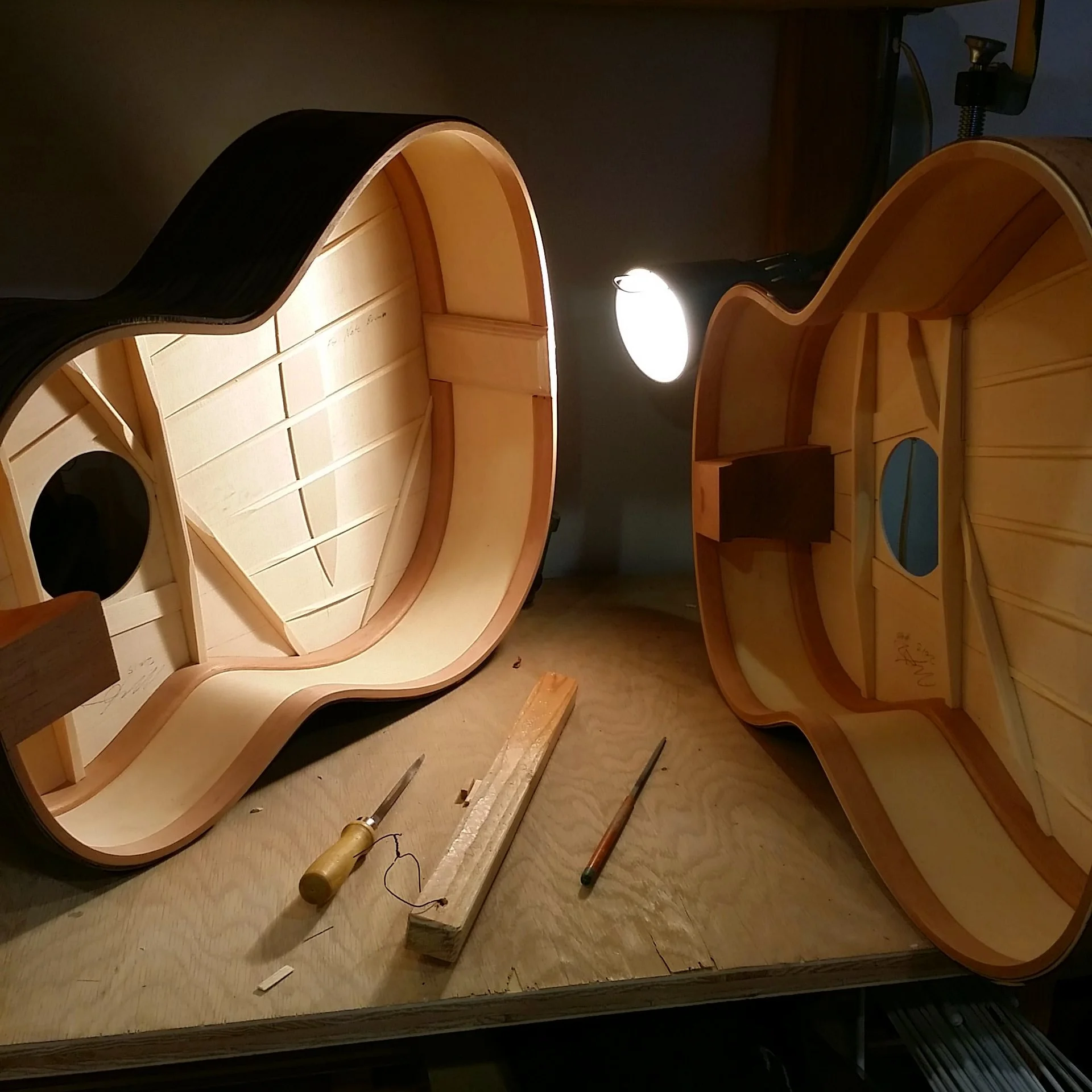 Two guitars with open backs on a workbench.