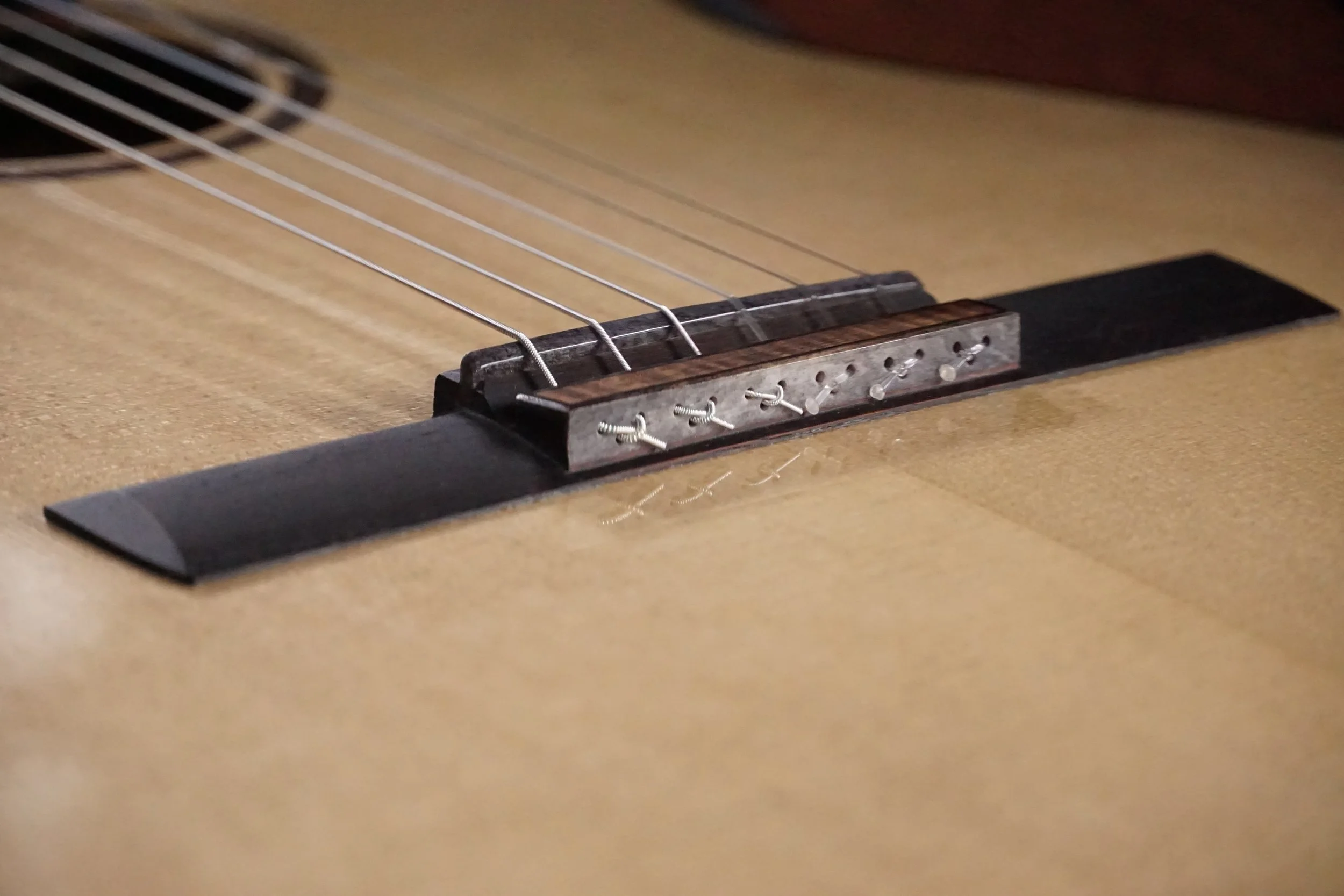 Close-up of an acoustic guitar's bridge, strings, and saddle on a wooden body.