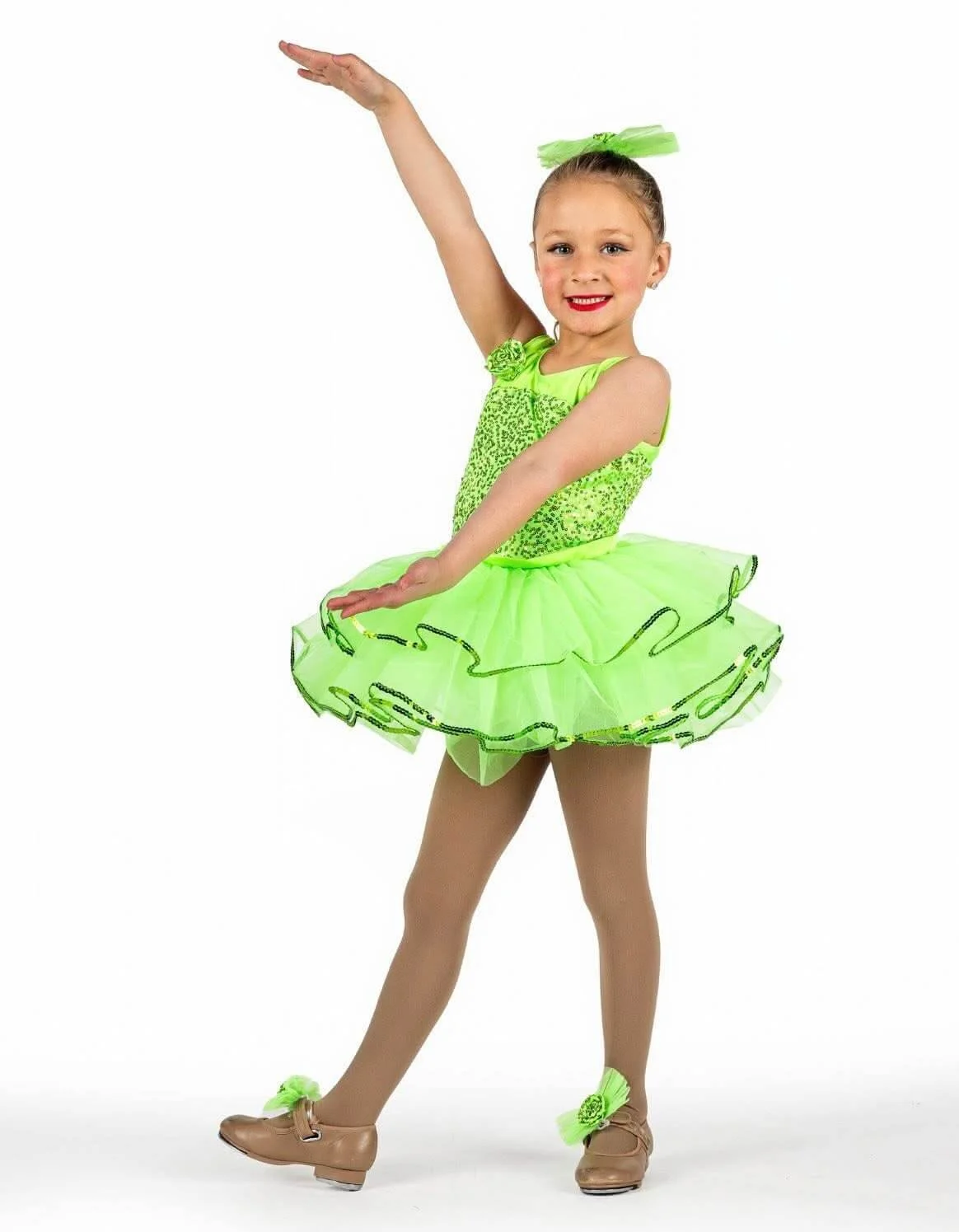 Young girl in bright green ballet costume, leaping on stage with arms raised, smiling, against a plain white background.