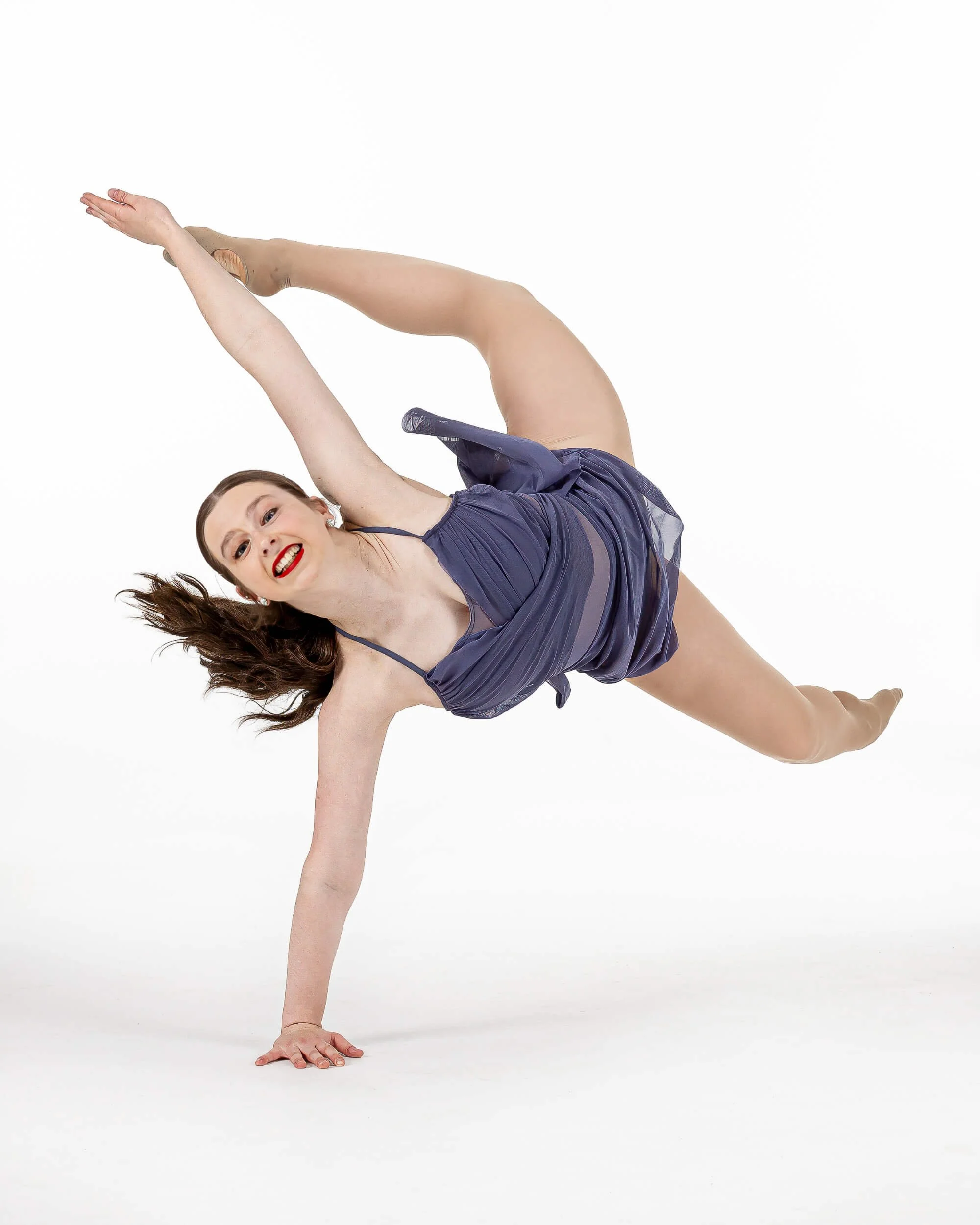 A woman in a purple dress performing a handstand in a studio with a white background.