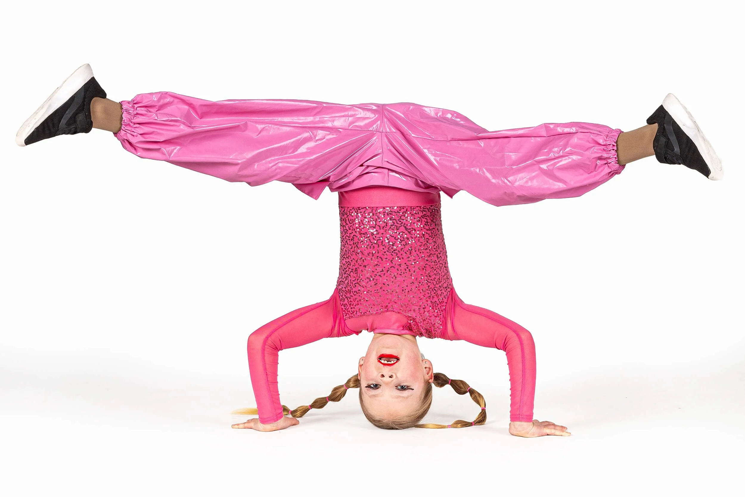 A young girl in pink dance costume balancing upside down in a handstand with legs spread wide apart