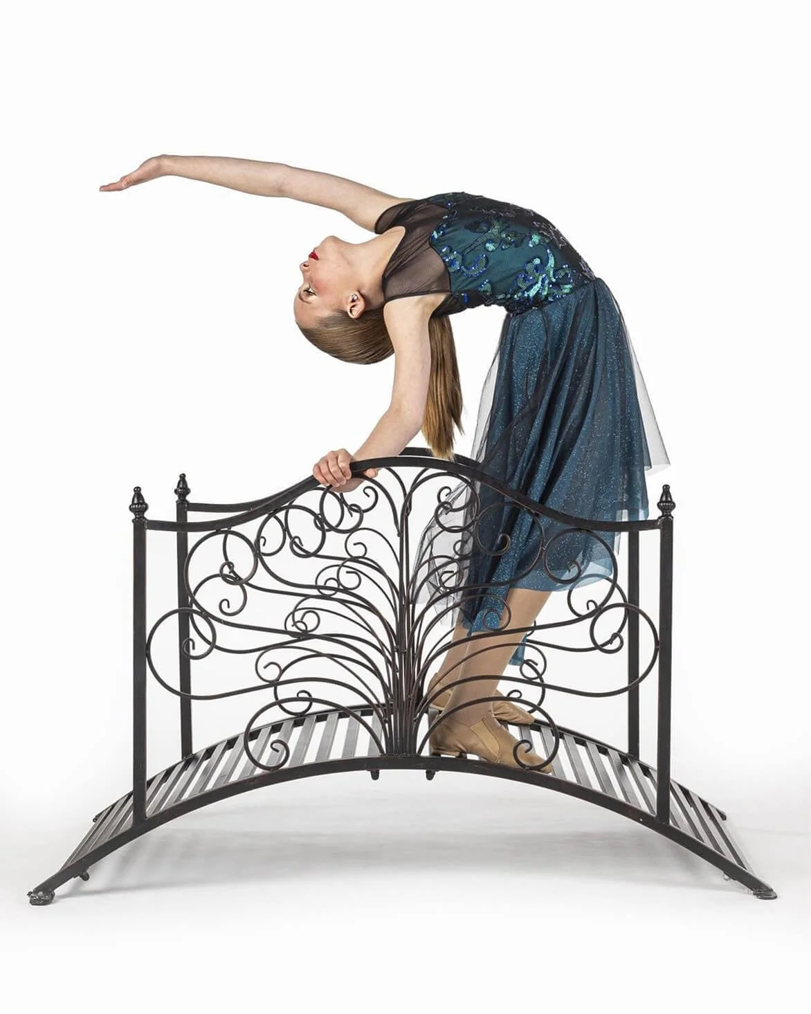 A woman in a blue dress stretching backwards while balancing on a decorative black metal gate.