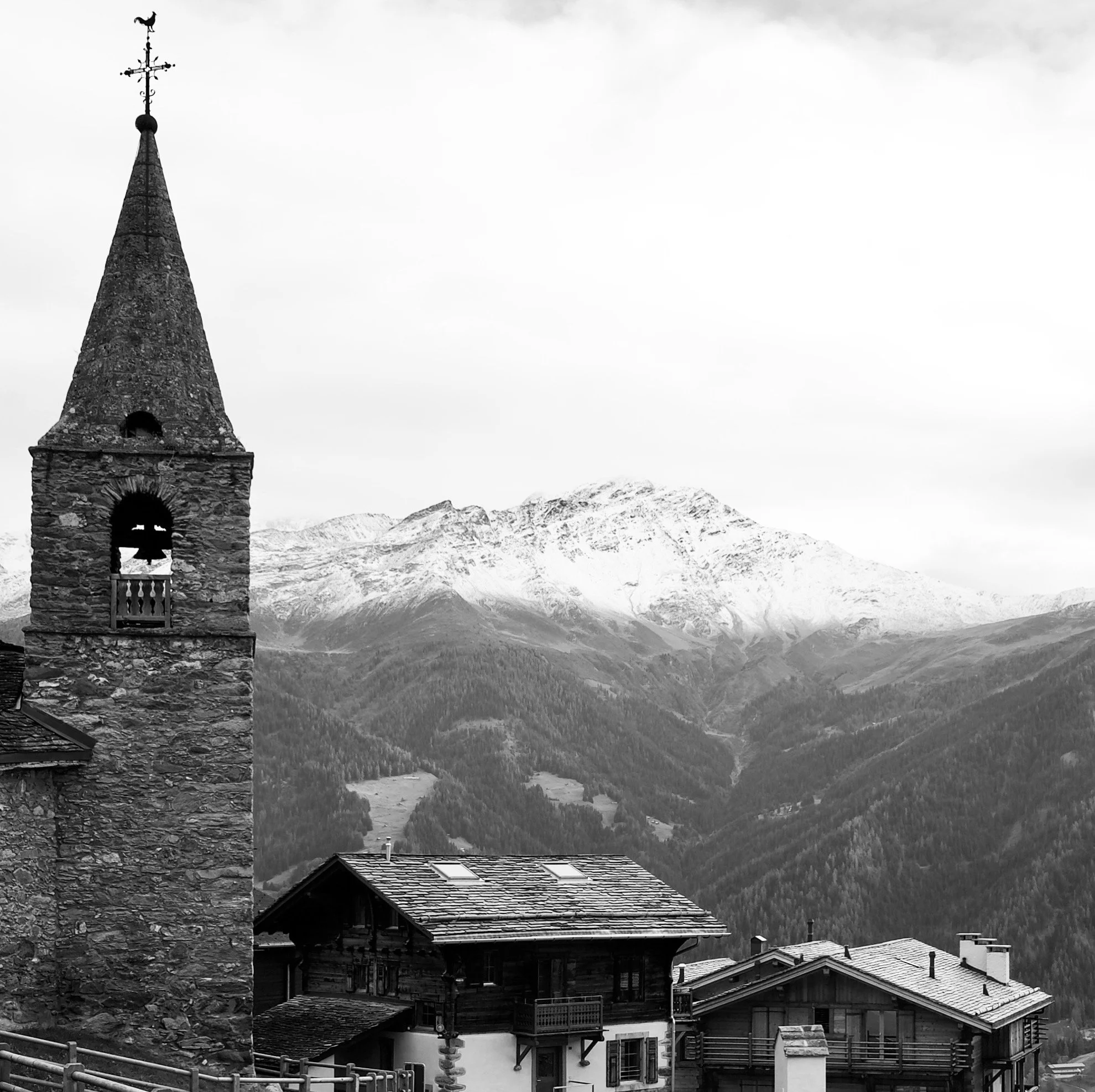 Paysage de montagnes enneigées avec des maisons en bois dans une vallée, et une tour d'église en pierre
