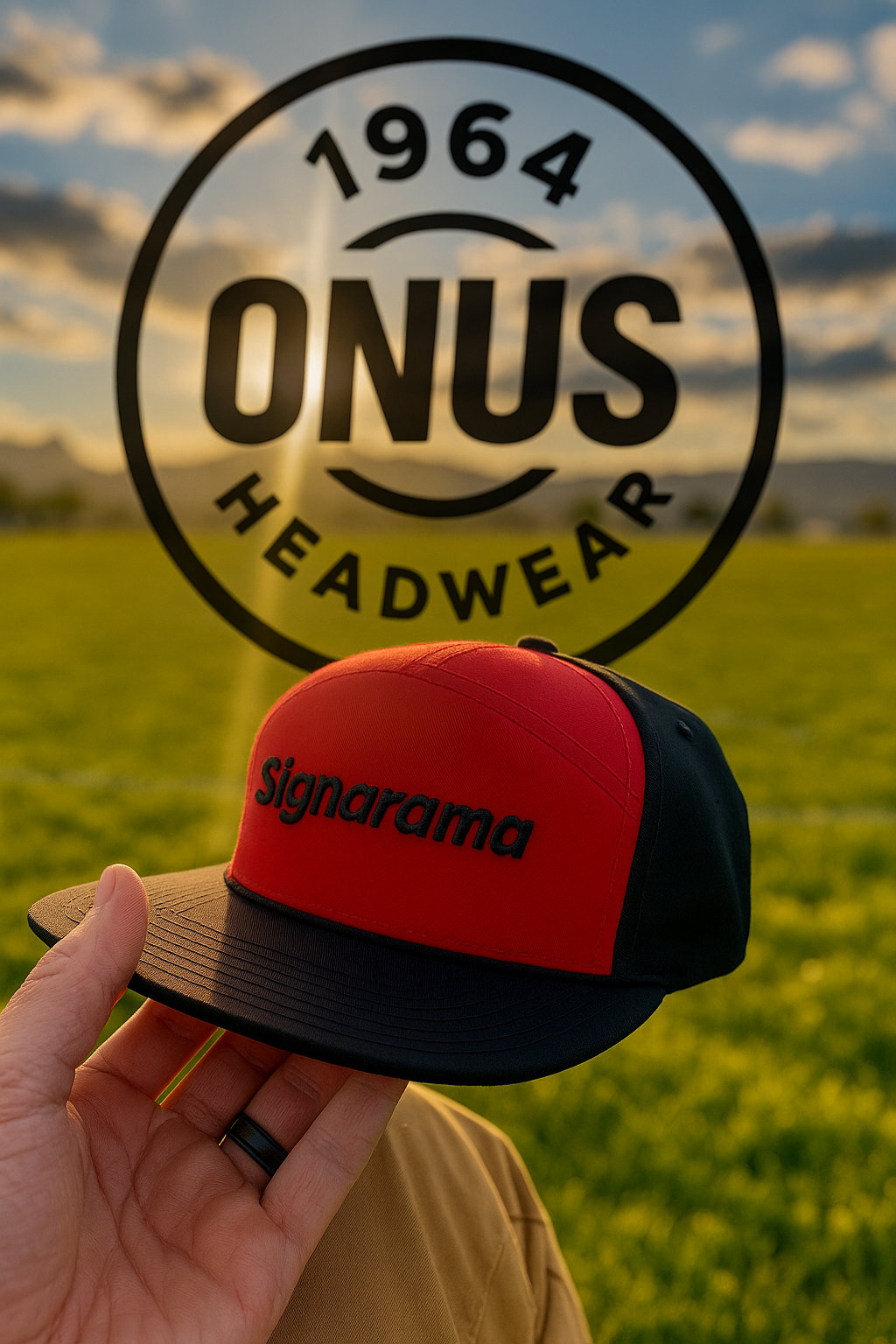 A person is holding a red and black Signarama baseball cap in front of a large transparent logo for ONUS Headwear, with a green field and a cloudy sky in the background.
