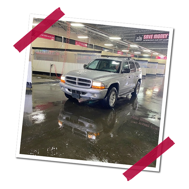 A silver SUV parked inside a wet parking garage with reflections on the floor, and pink promotional signs hanging overhead.