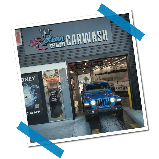 A blue Jeep at a car wash entrance with a sign that reads 'Clean Getaway Car Wash'.