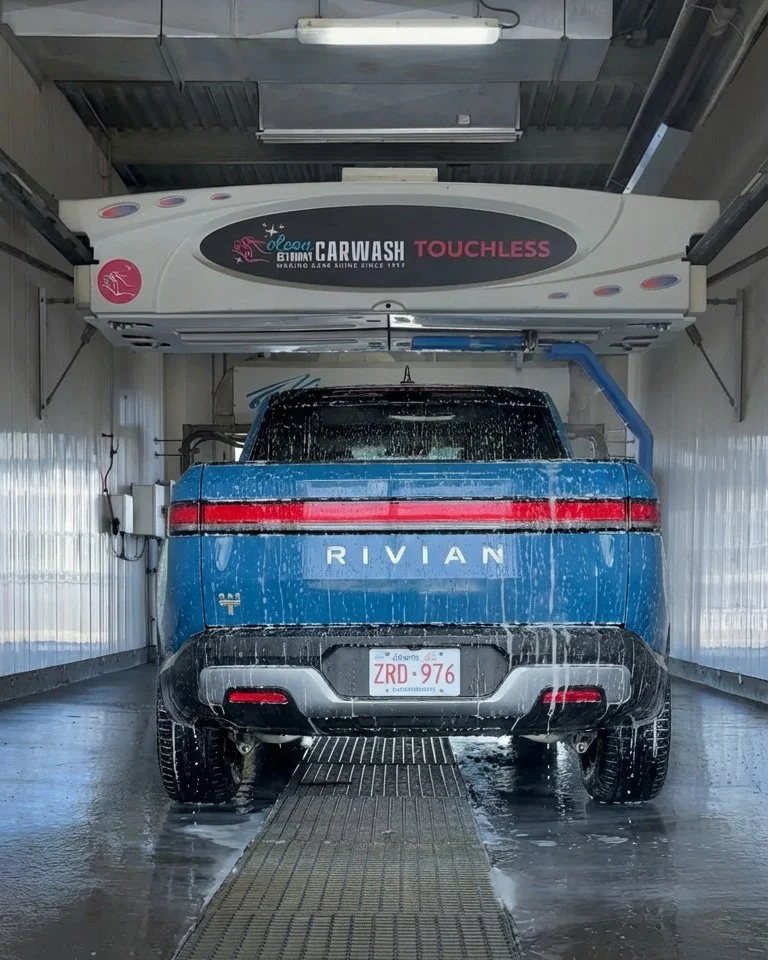 A blue Rivian electric pickup truck inside an automatic car wash, with water and soap on the vehicle.