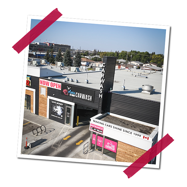 Exterior view of a car wash business with a sign that reads 'Now Open' and 'Clean Car Wash,' featuring a black and pink color scheme, and slogans 'Making cars shine since 1999' and 'Save money' on the storefront.