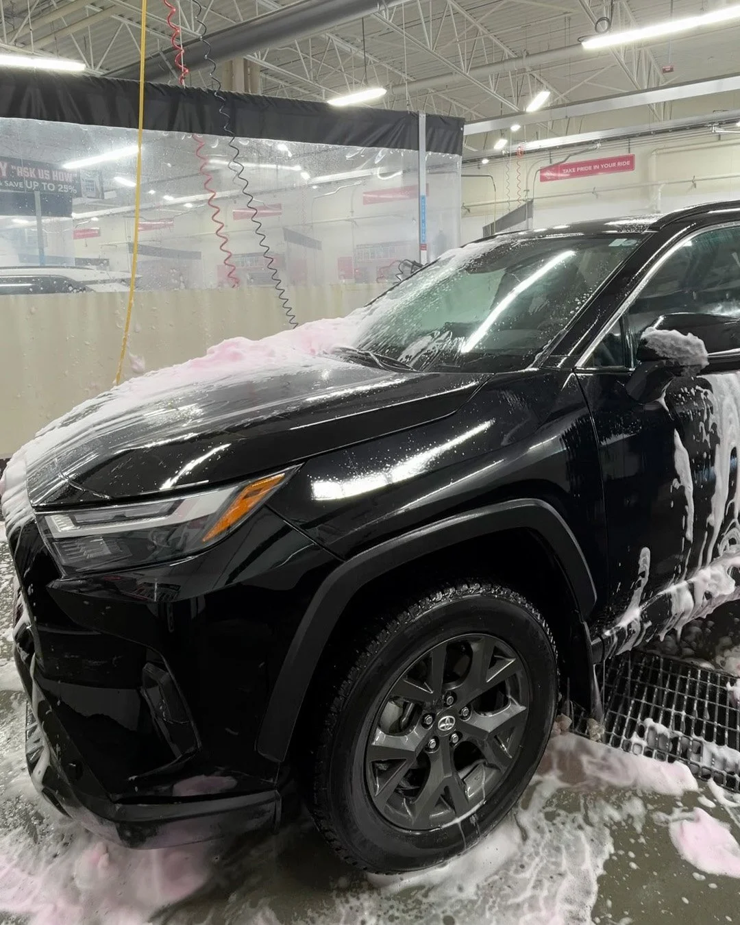 A black SUV at an automatic car wash being washed with soap and foam.
